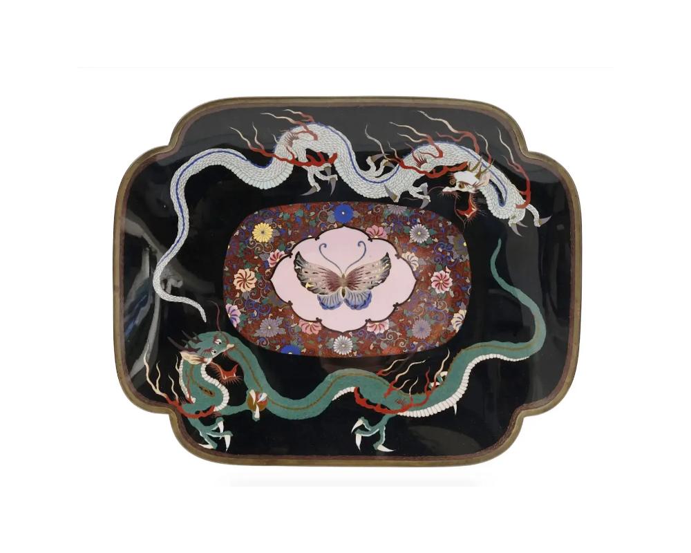 A large antique Japanese, late Meiji era, enamel over brass tray. The tray is enameled with a polychrome medallion depicting a butterfly surrounded by floral and foliage patterns, and images of dragons on a black ground made in the Cloisonne