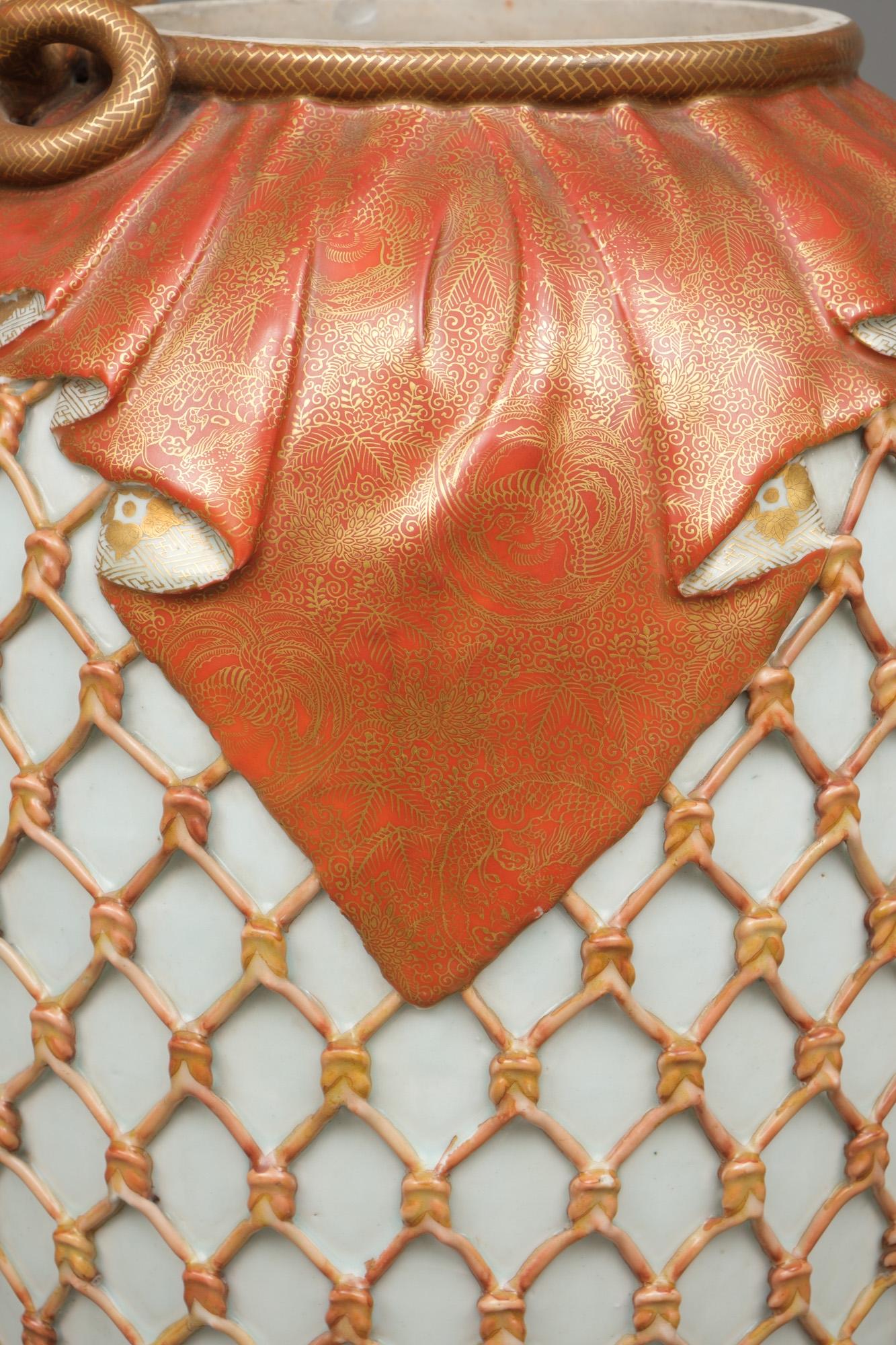 Grande jarre (tsubo) en porcelaine de Kyo d'une facture exceptionnelle, ornée d'un motif en relief d'inspiration naturaliste représentant un filet de couleur corail tendu autour du corps. Sur l'épaule est suspendue une magnifique étoffe glacée rouge