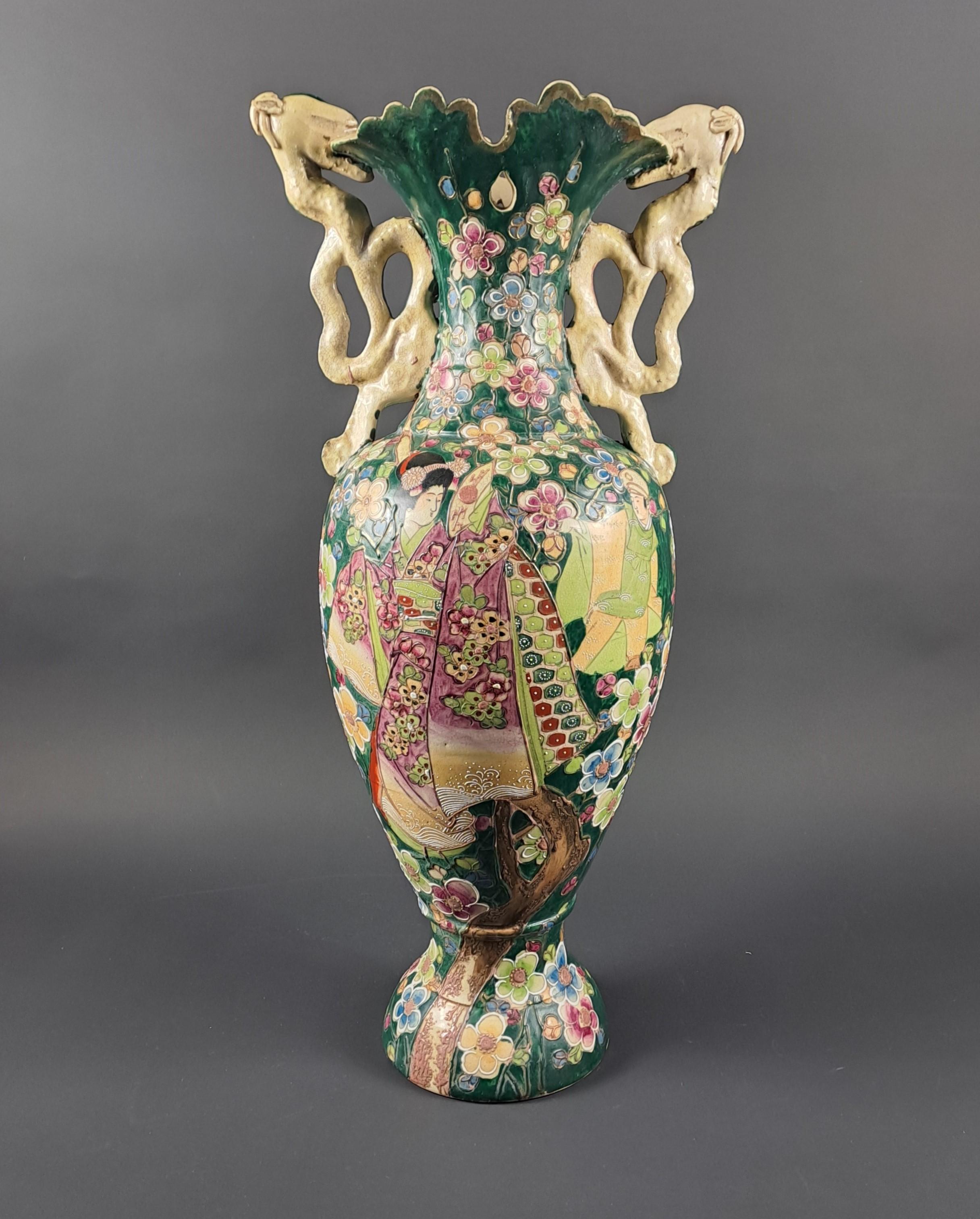 Grand vase en porcelaine japonaise représentant une scène de séduction entre une geisha et un personnage masculin dans un riche décor floral et végétal polychrome aux couleurs vertes dominantes.  

 Grandes poignées en forme de dragon mordant le