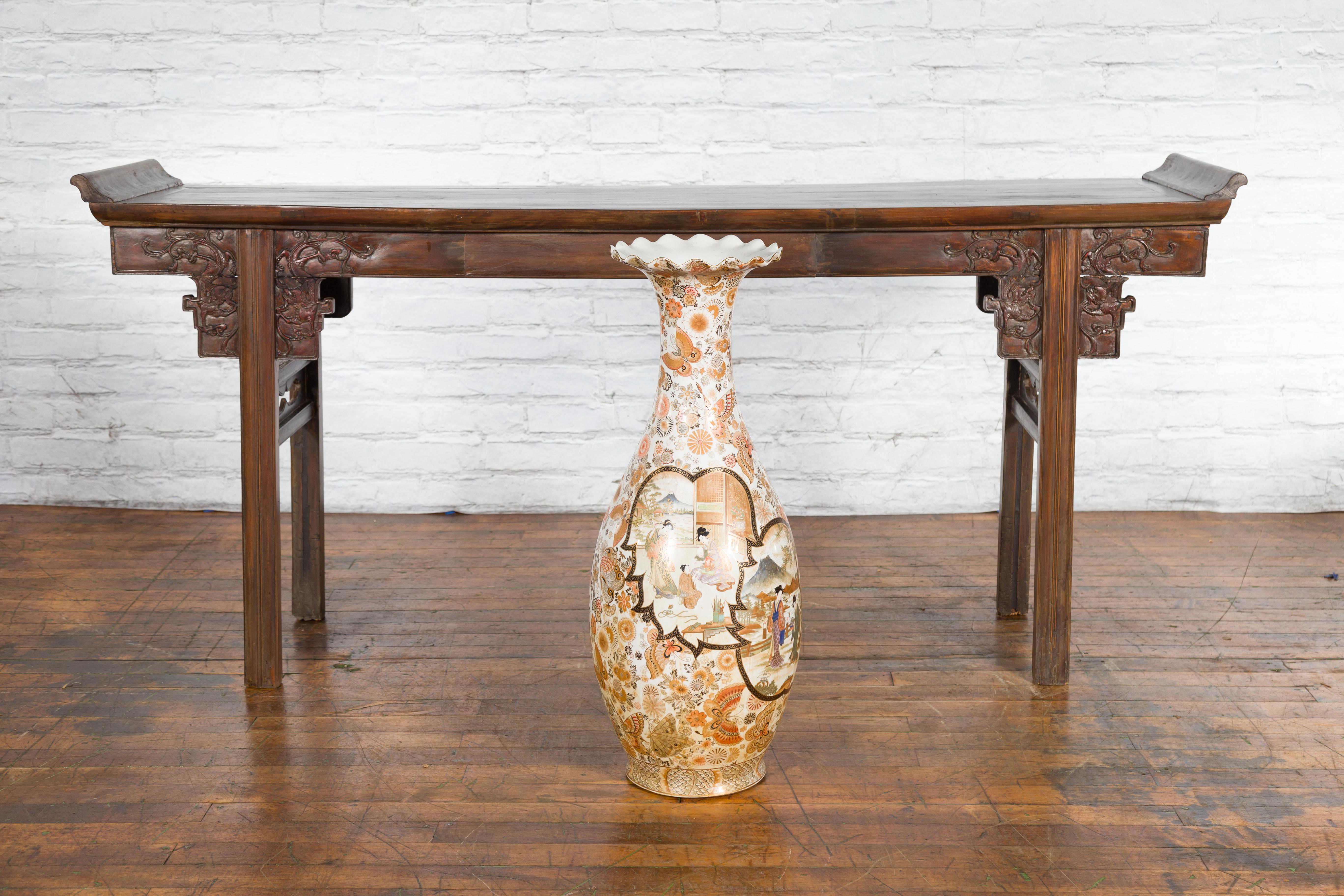 A large Japanese vintage Kutani style palace vase from the mid-20th century, with court scenes and scalloped top. Created in Japan during the midcentury period, this Kutani style palace vase features a scalloped top sitting above an orange, gold and