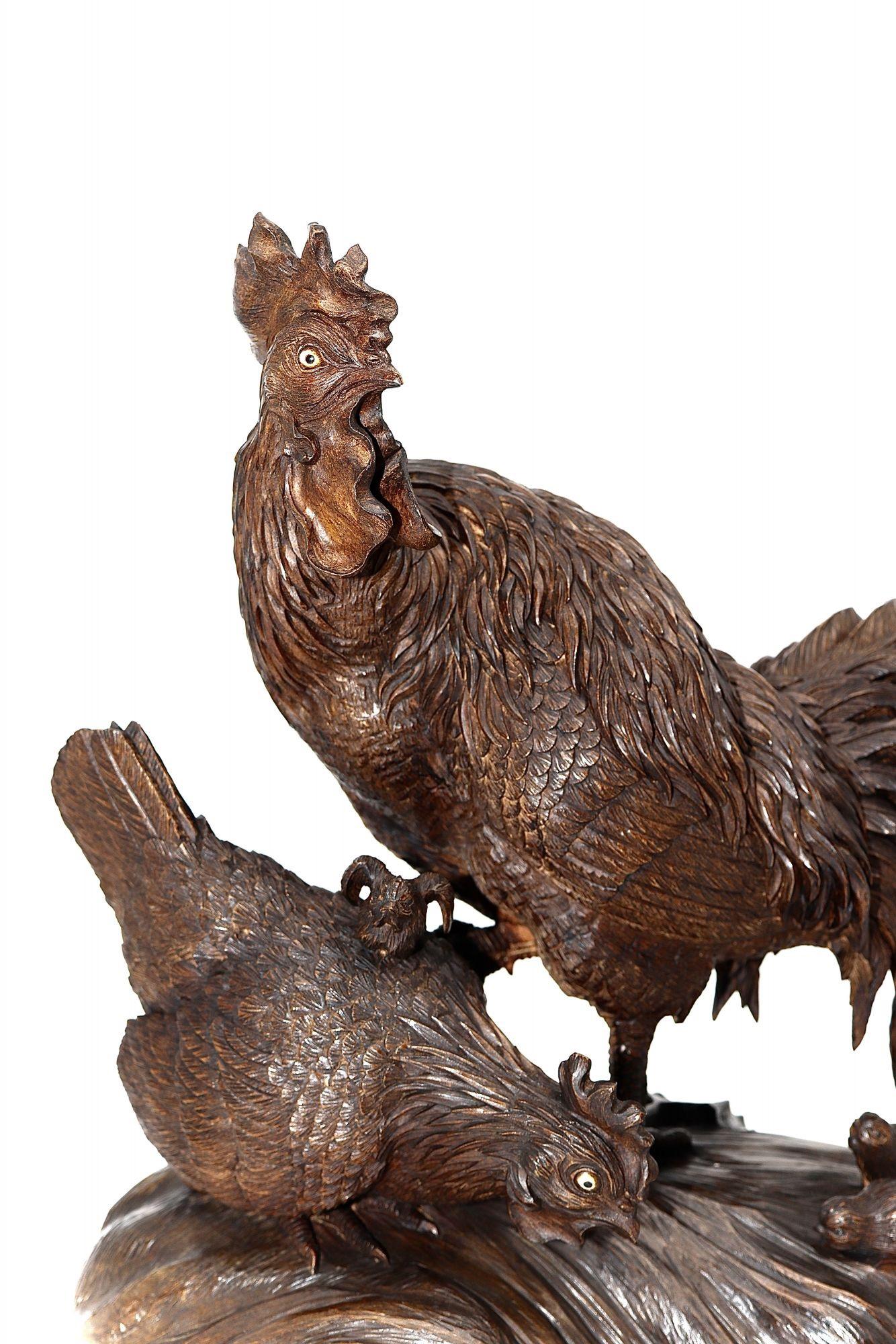 A finely signed Japanese carved large cockerel with an impressive plume of tail feathers standing over his family consisting of a hen and baby chicks as they pick at the ground searching for food. The details finely wrought and highlighted with