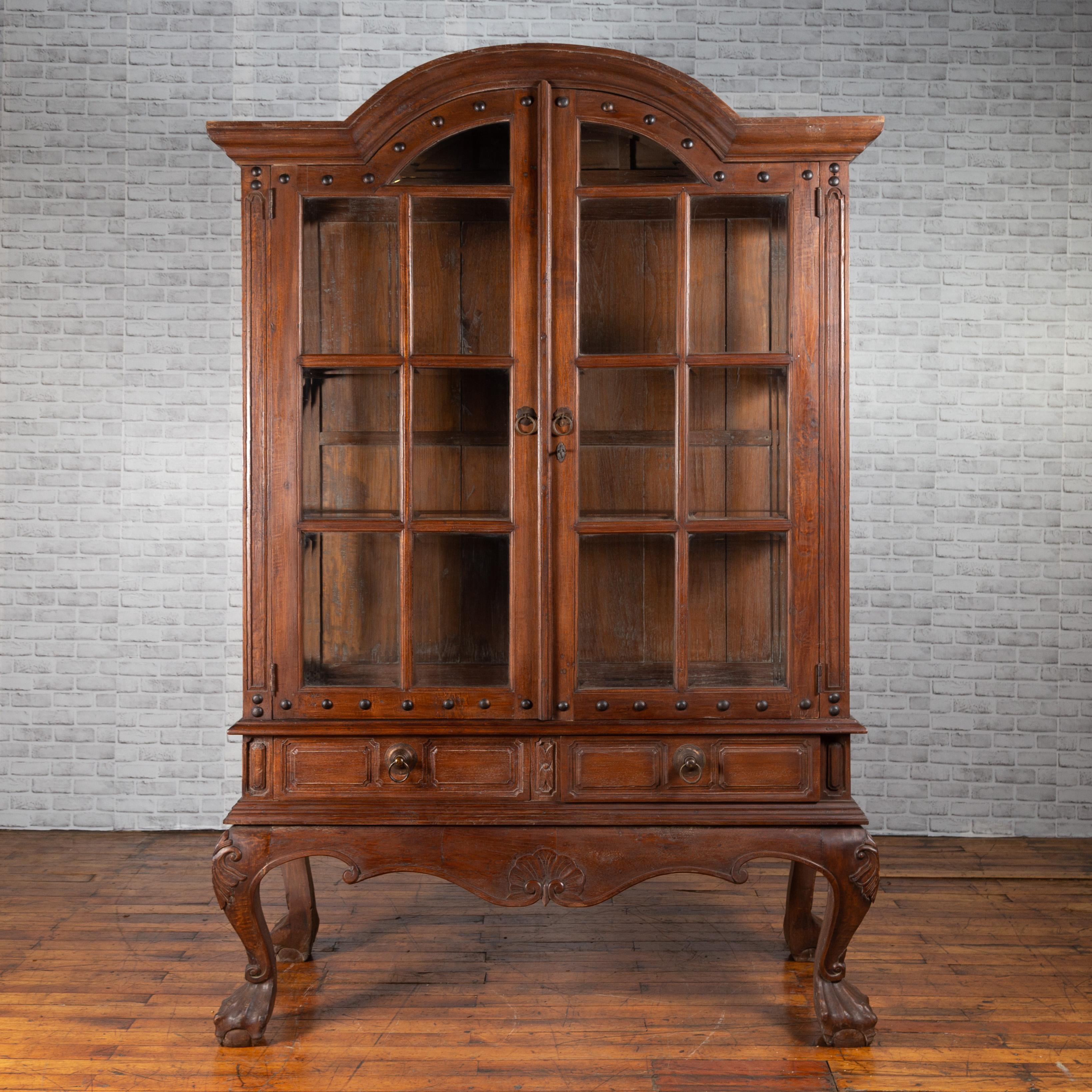 A large Dutch Colonial cabinet from Java with bonnet top, double glass doors and sides. Created in Java during the early 20th century, this large cabinet features an exquisite bonnet top, sitting above a pair of double doors with paneled glass and