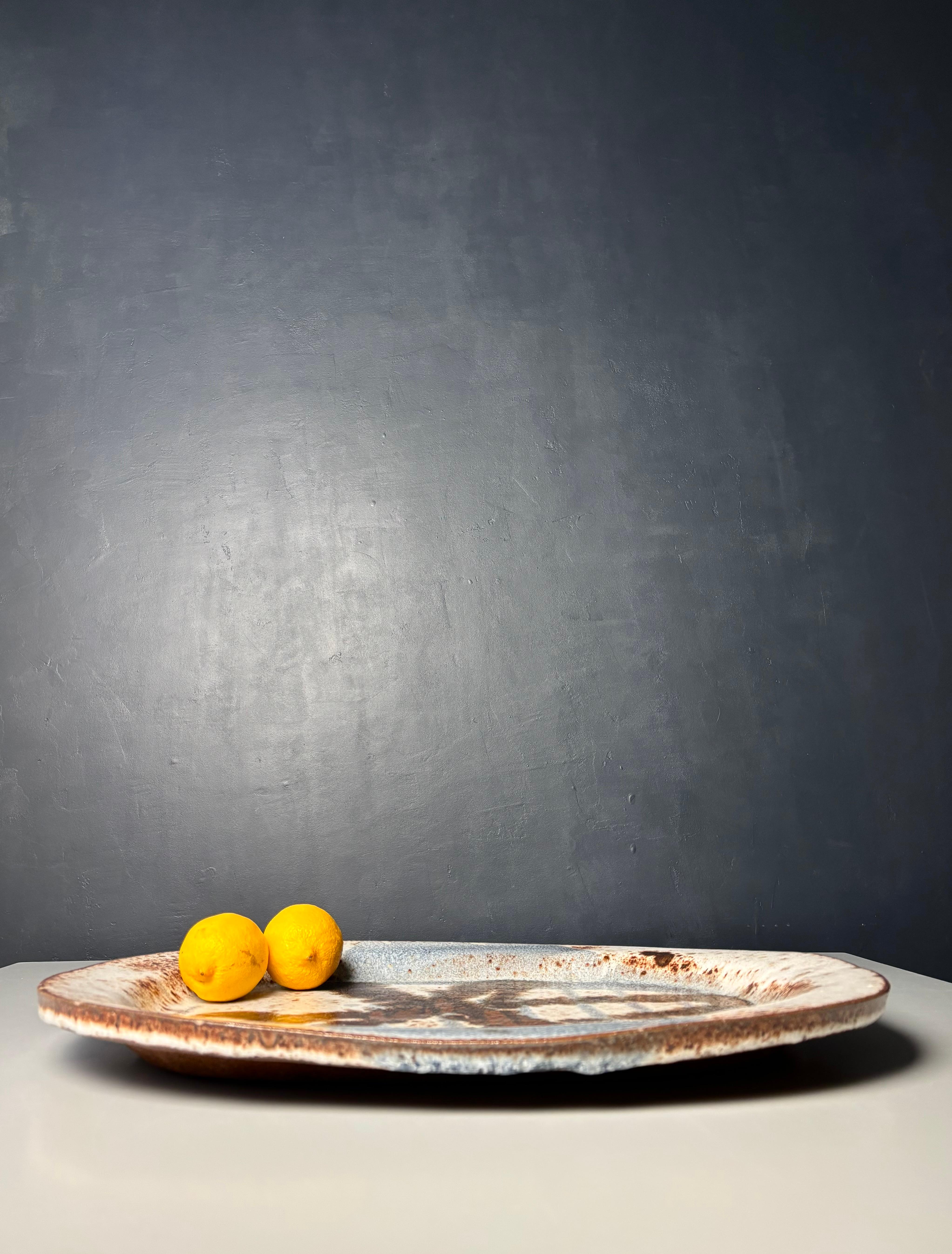 Large ceramic centerpiece handmade by Danish artist Jørgen Finn Petersen in the 1960s. Ellipse shaped dish making the item usable as a decorative dish, a centerpiece, or as a wall art piece. Abstract decoration in hand-painted spotted glaze in warm