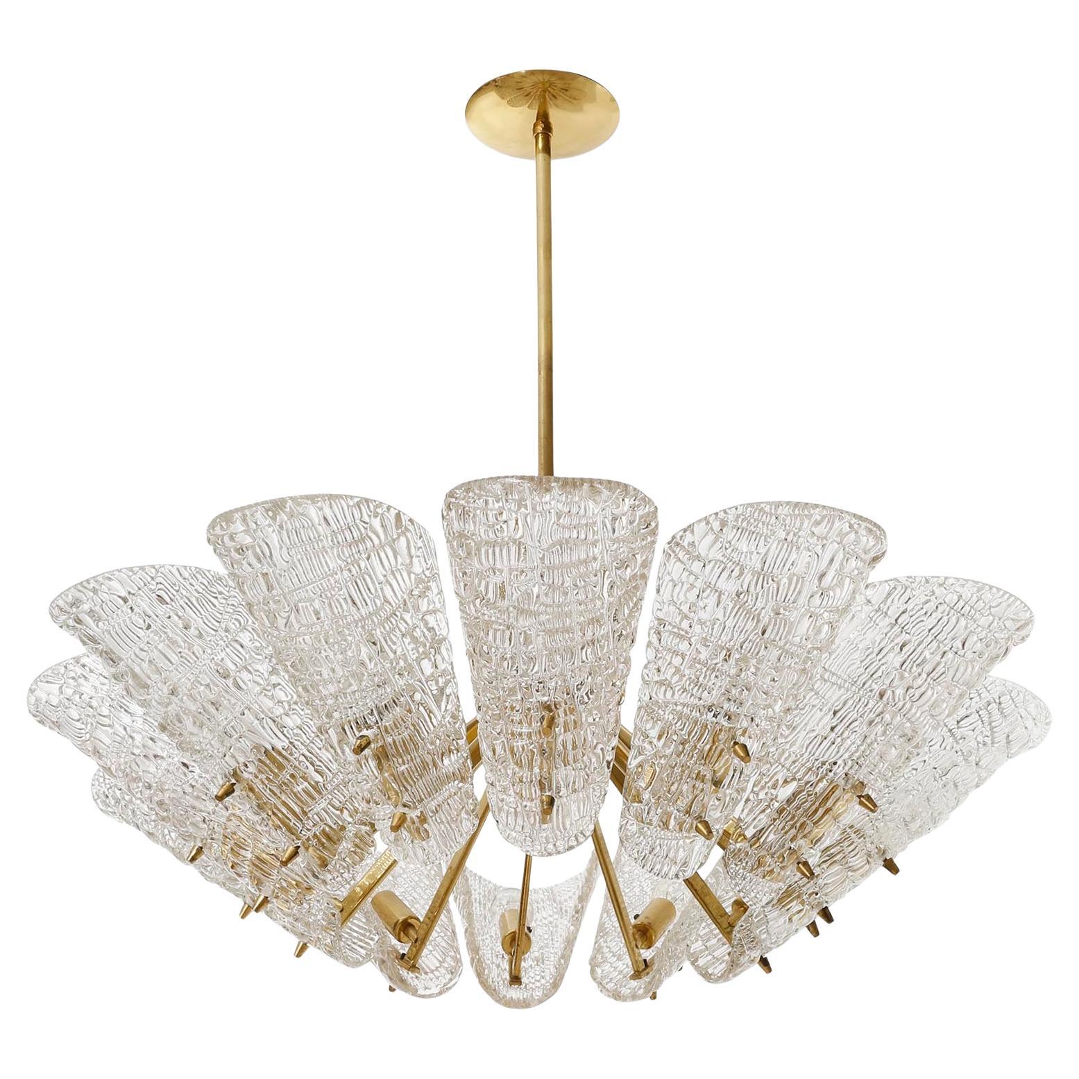 A large glass and brass chandelier by J.T. Kalmar, Vienna, Austria, manufactured in midcentury, circa 1960 (late 1950s or early 1960s).
The fixture is made of a black painted metal center piece which holds 12 arms made of solid polished brass which