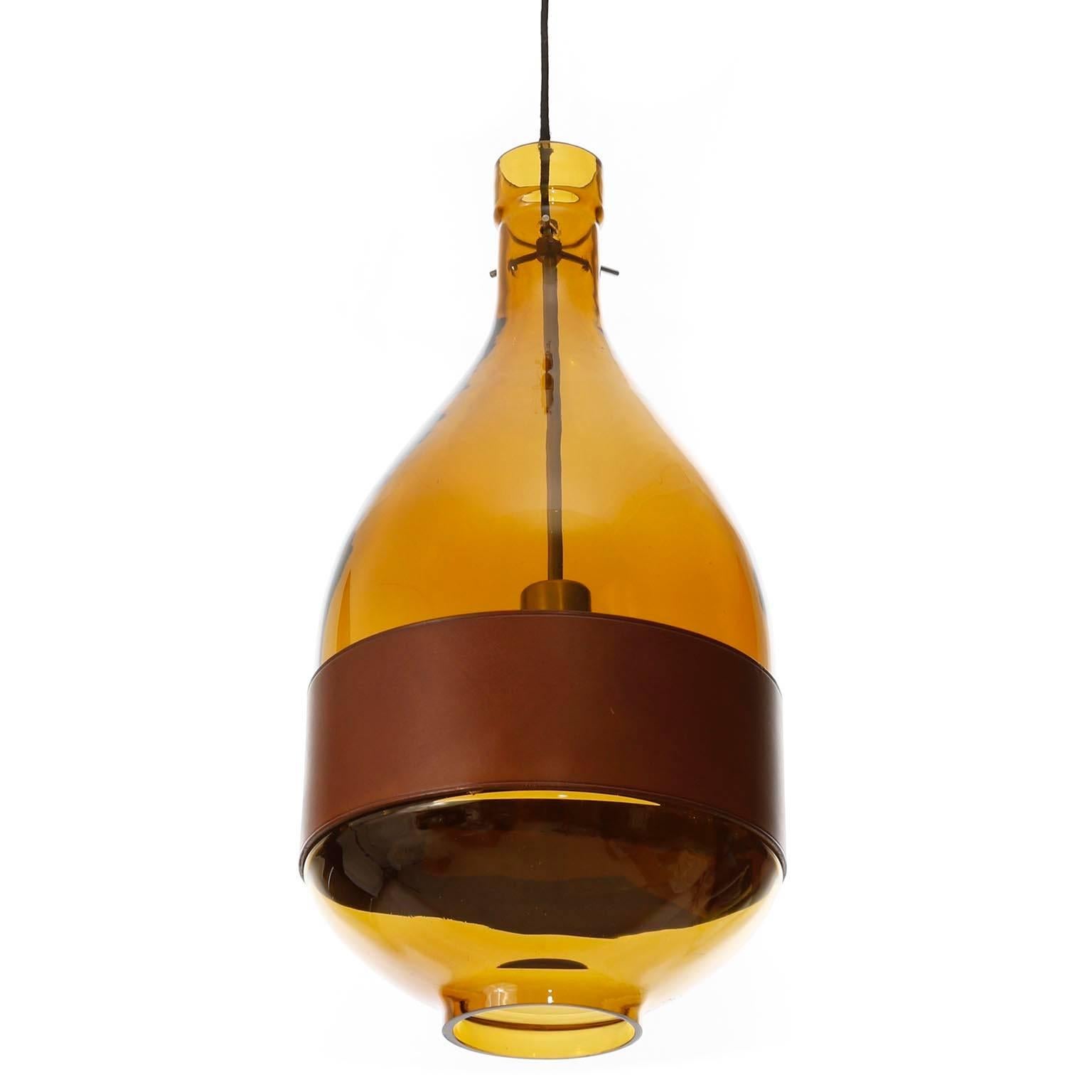 A beautiful glass pendant light fixture by Kalmar, manufactured in Mid-Century, circa 1970 (late 1960s or early 1970s). 
It is made of an hand blown amber toned glass body with a belt made of brown leather.
The dimensions of the glass body without