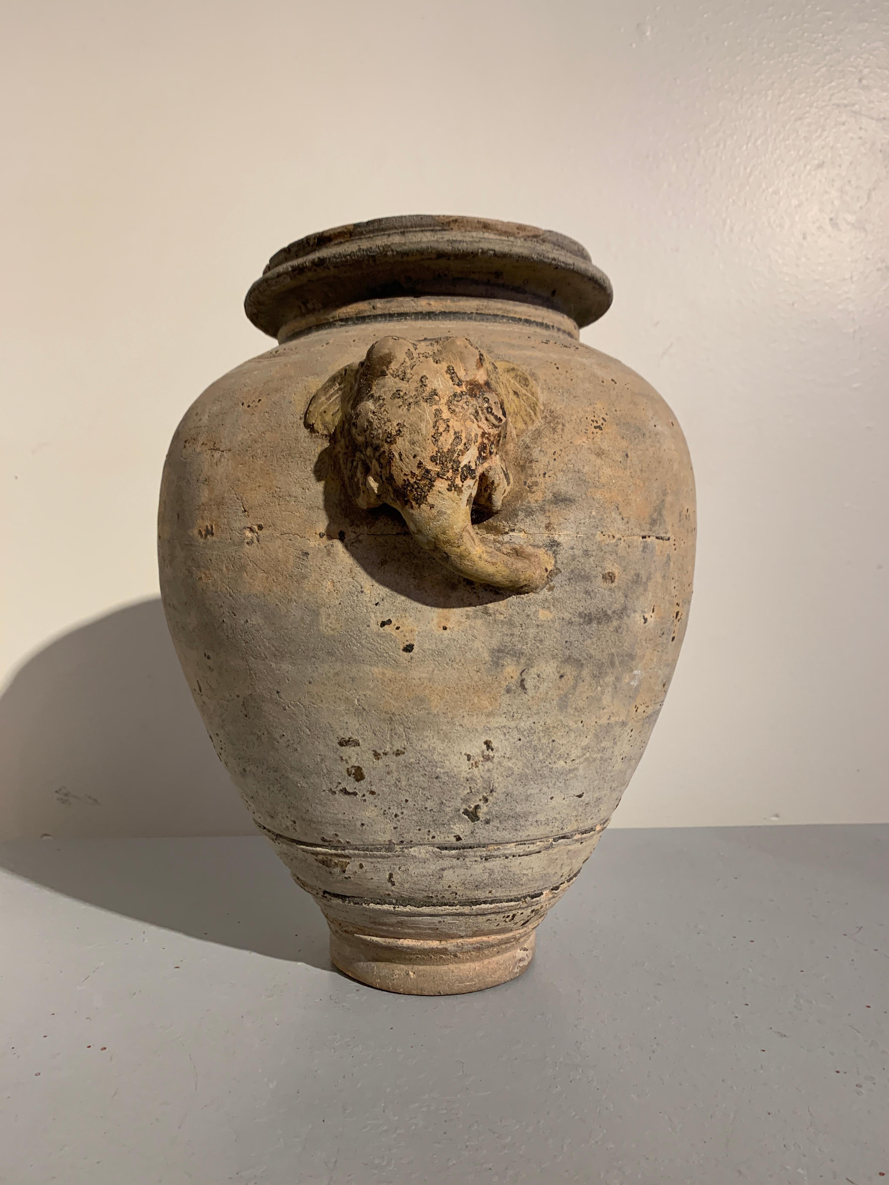 A large and fanciful Khmer buff pottery jar with applied elephant head and tail, 16th century, Cambodia.

The tall and heavy vase, jar, or vessel of ovoid shape, set on a tall, narrow foot, and featuring a short neck supporting a wide, everted