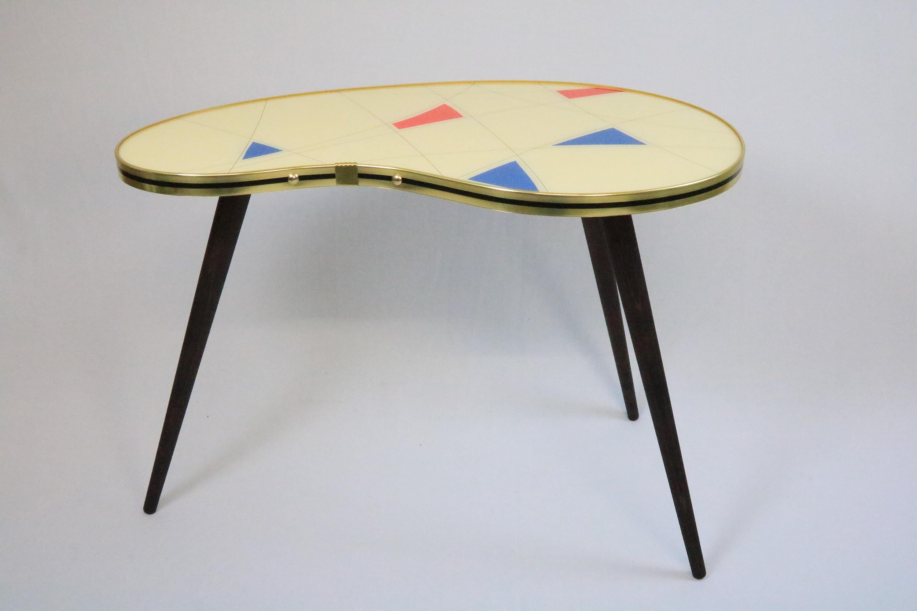 High quality kidney shaped table produced in local Berlin workshops. 
With decorative geometric pattern in typical 50s Design. (More forms and patterns in other offers) 
Brass line. 
Three wooden legs, dark stained and waxed. 
Top made of wood and