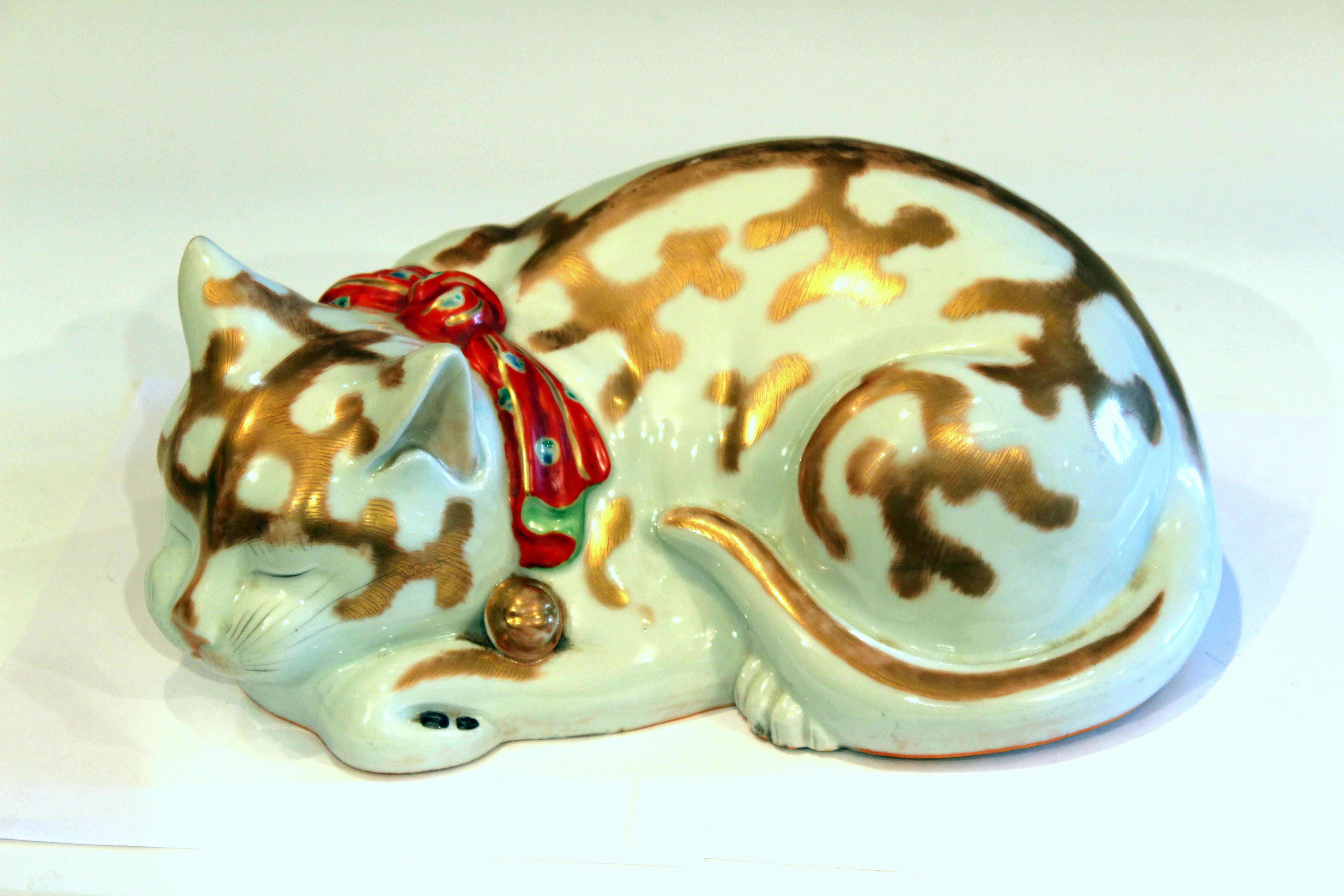 Japanese Kutani porcelain cat figure peacefully curled in sleep with finely painted detail, gilt highlights, and bright red bow, circa 1920s. Large life like size. Export stamp on base. Measures: 13