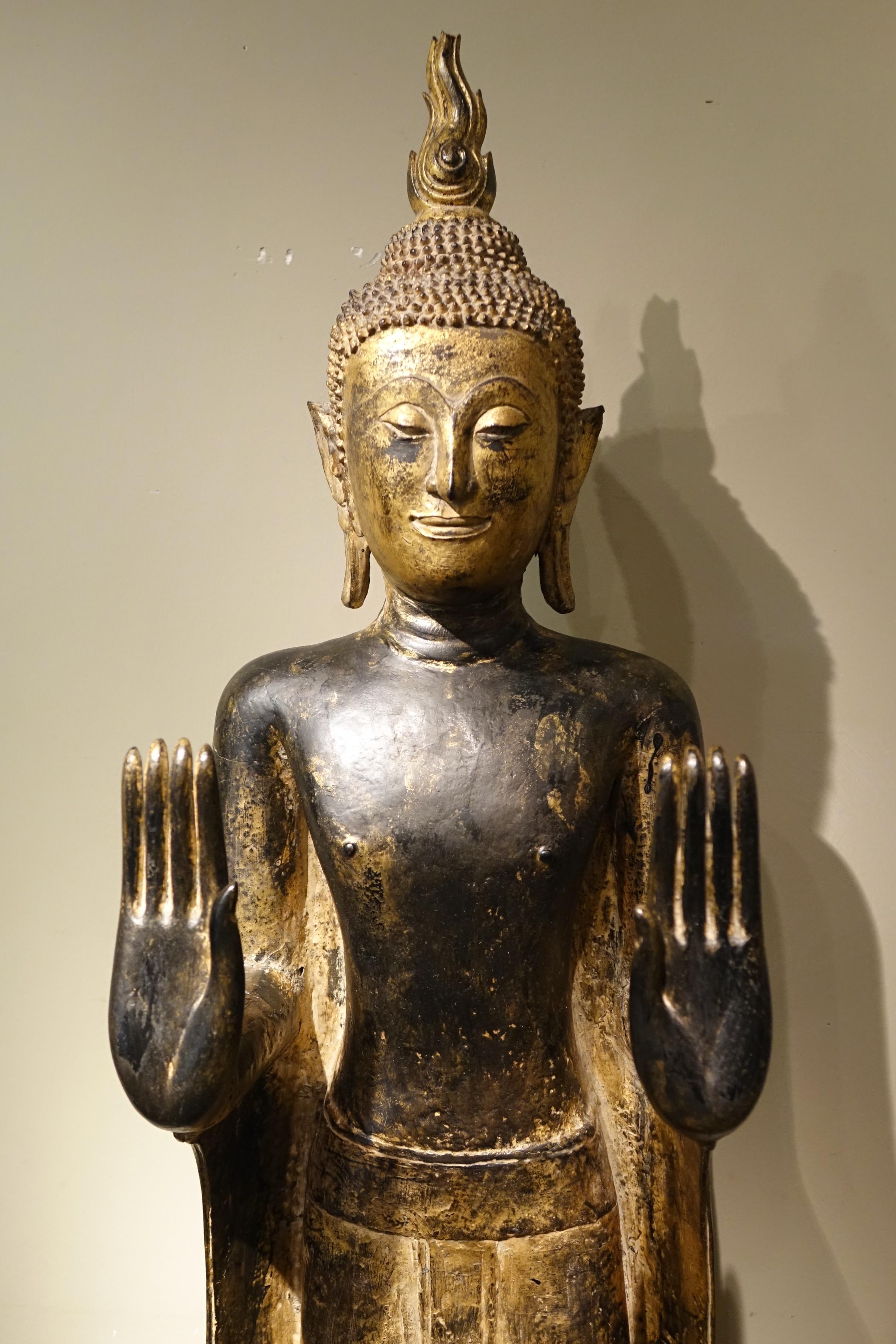 Standing Buddha, large size, in lacquered and gilded wood, in the abhaya mudrà gesture of absence of fear and protection.
This gesture evokes the episode when Buddha was attacked by a furious elephant in the streets of Rajagarha. The animal,