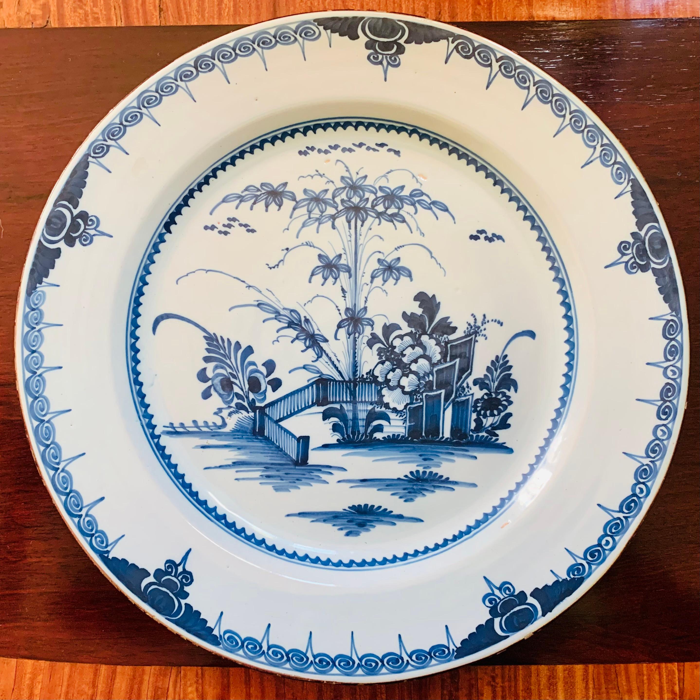 A large blue and white charger decorated with a Chinese inspired garden and fence vignette, and a repeating scroll pattern border with a brown glazed rim. An identical example is in the collection of the Victoria and Albert Museum, attributed to