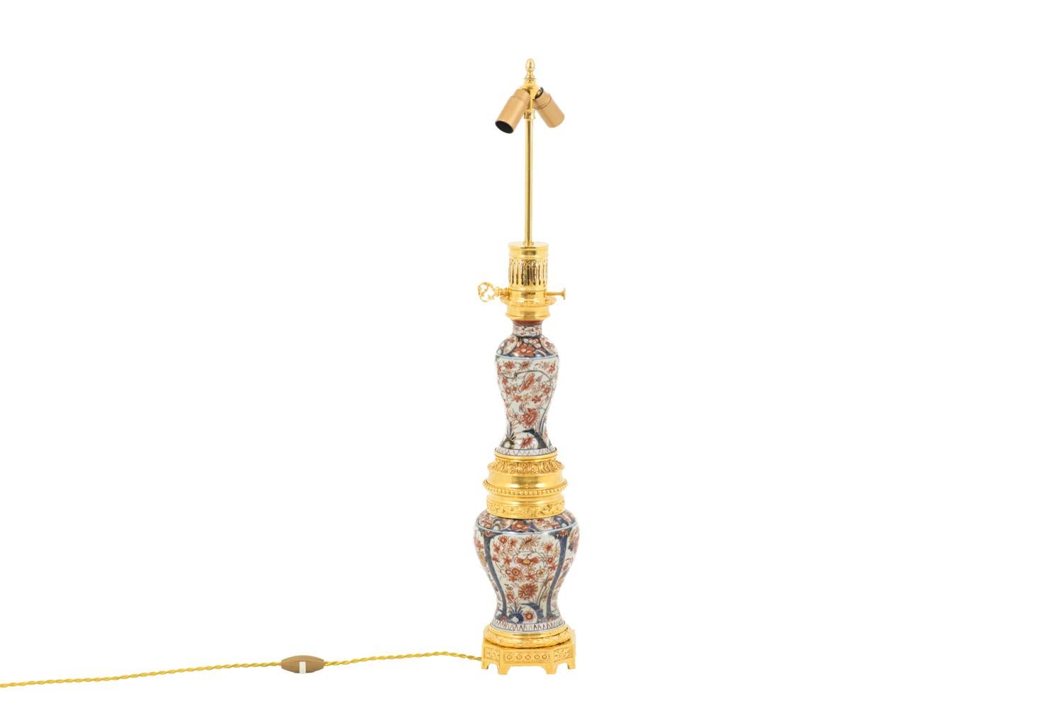 Large lamp in Imari porcelain formed by two balusters. Imari decor in the blue and red tones with gilt highlights on a white background figuring flowers in large cartouches.
Chiselled and gilt bronze mount. Top of the mount with an openwork decor