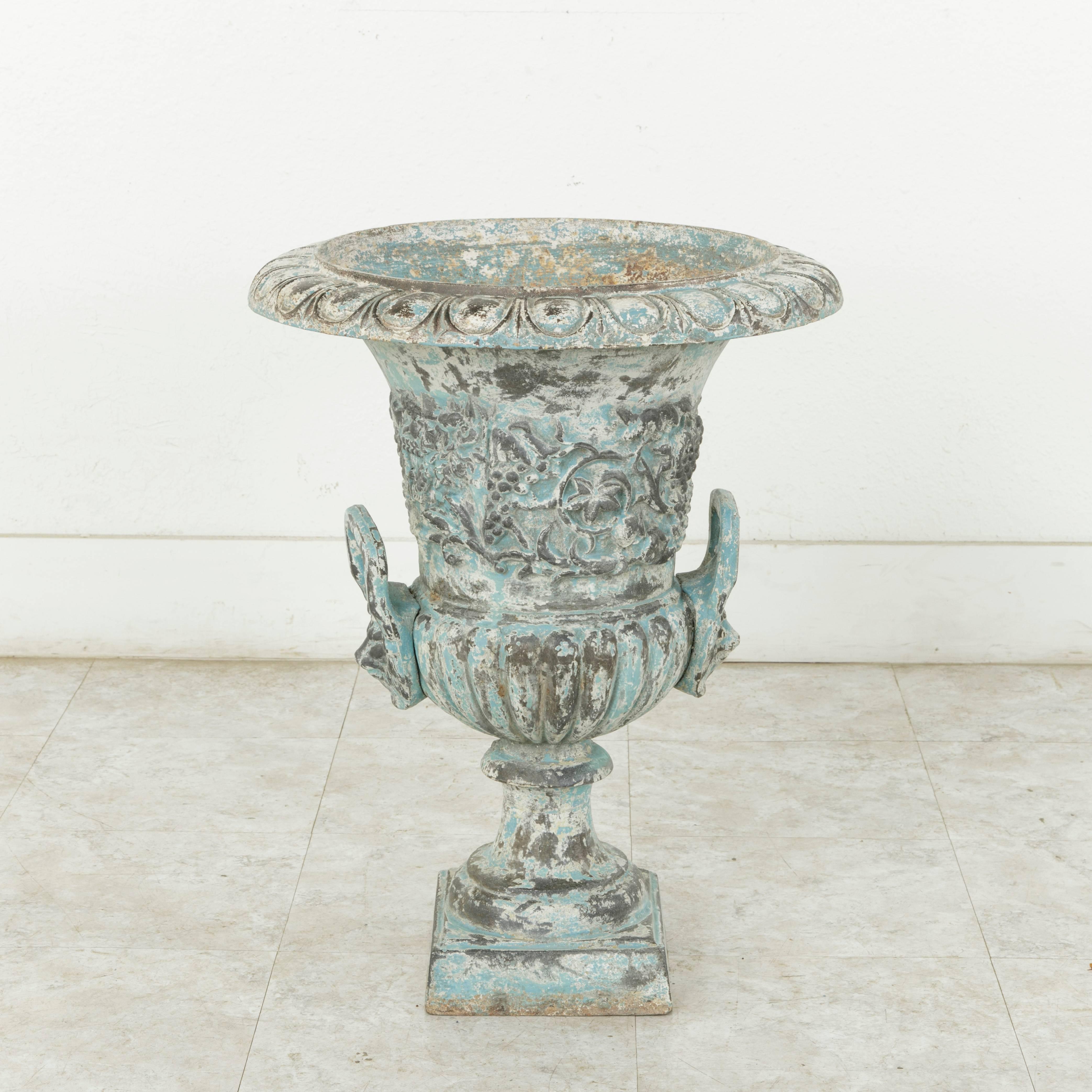 Standing almost 25 inches in height, this large late 18th century French cast iron urn or planter features motifs of grapes, vines, and grape leaves, indicative of its origin in a French vineyard. Each handle bears the head of a lion wearing a
