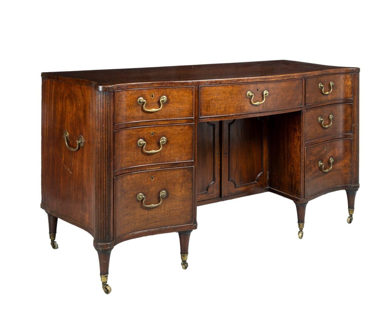 A large late 18th century Hepplewhite figured Mahogany serpentine kneehole desk with shaped square edge top above two banks of three graduated drawers, large fitted centre drawer above a kneehole and a panelled cupboard beneath; reeded side columns,