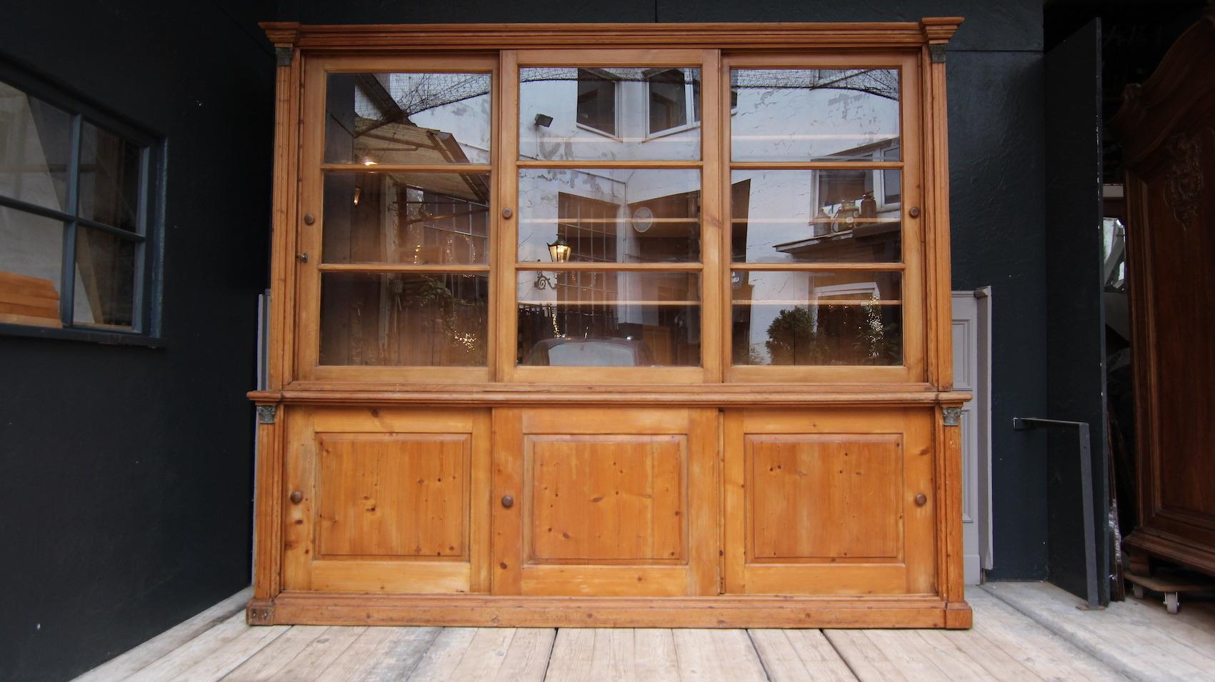 Large English shop display cabinet, made of solid pine and waxed, circa 1880.
Consisting of a lower part with 3 sliding doors and an upper part with 3 glazed sliding doors behind which there are a total of 8 adjustable shelves. Corinthian capitals
