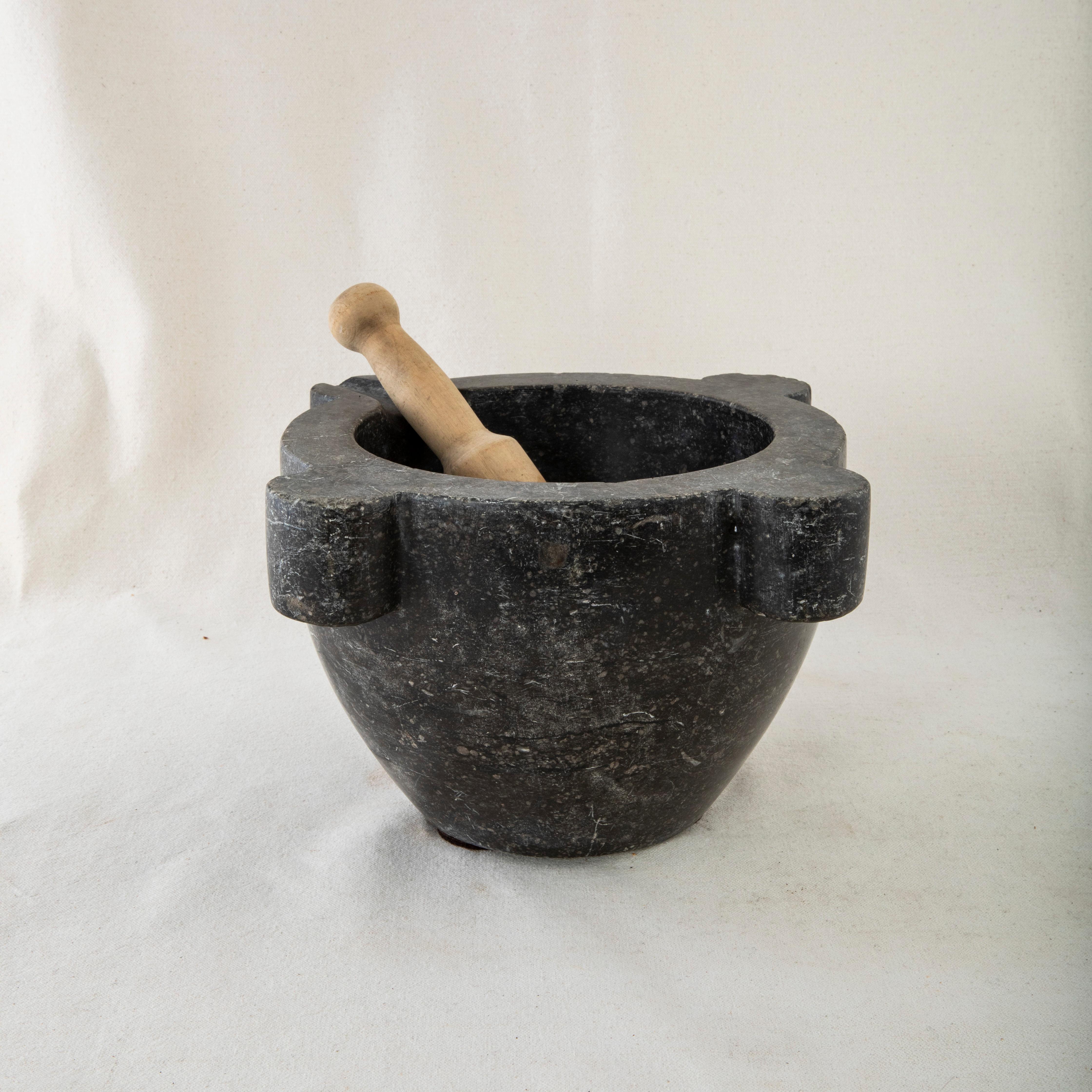 This large black marble mortar from the nineteenth century is made from a single block of marble and features its original turned pestle made of wood. Once used by a pharmacist to grind herbs for medicinal purposes, it can now serve as a planter,