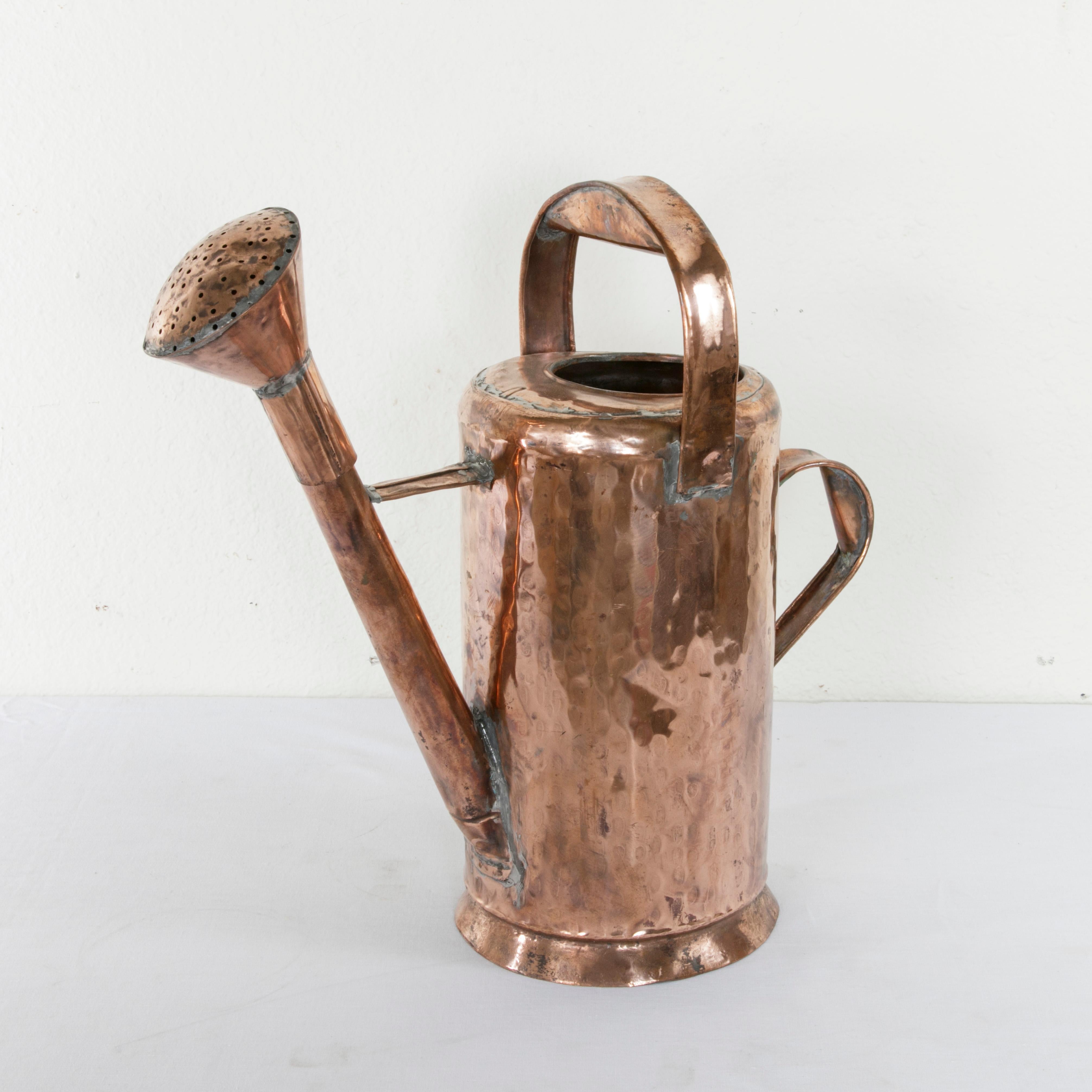 This large scale French hand-hammered copper watering can from the late 19th century features a tall cylindrical form. The piece is fitted with two handles to allow for easier pouring. A pierced copper rose at the end of its spout is removable. A