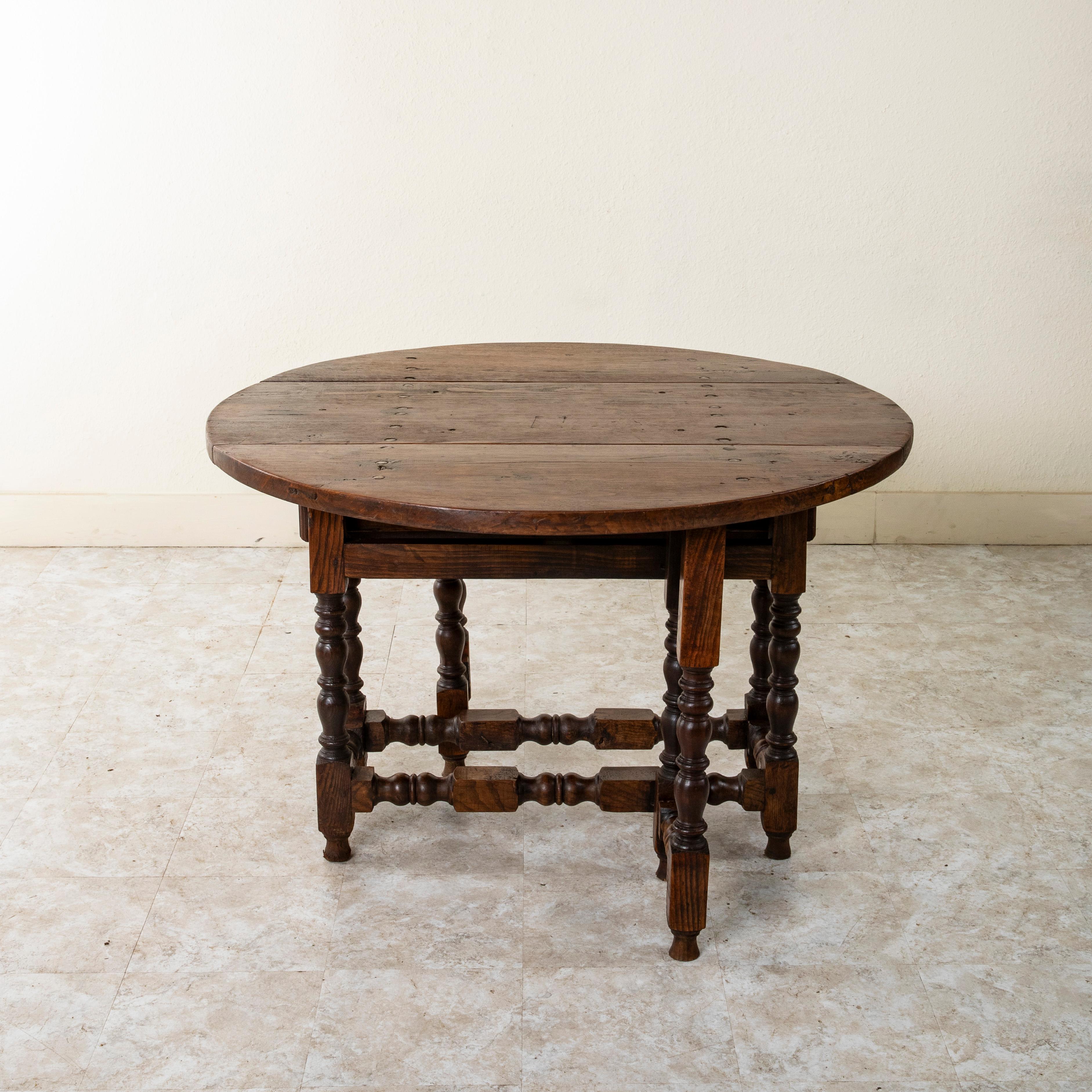 Found in the city or Perpignan, on the Spanish border in southern France, this large late nineteenth century oak gateleg table features a 47 inch diameter top with two drop leaves. The top is detailed with hand forged iron nails and each end of the