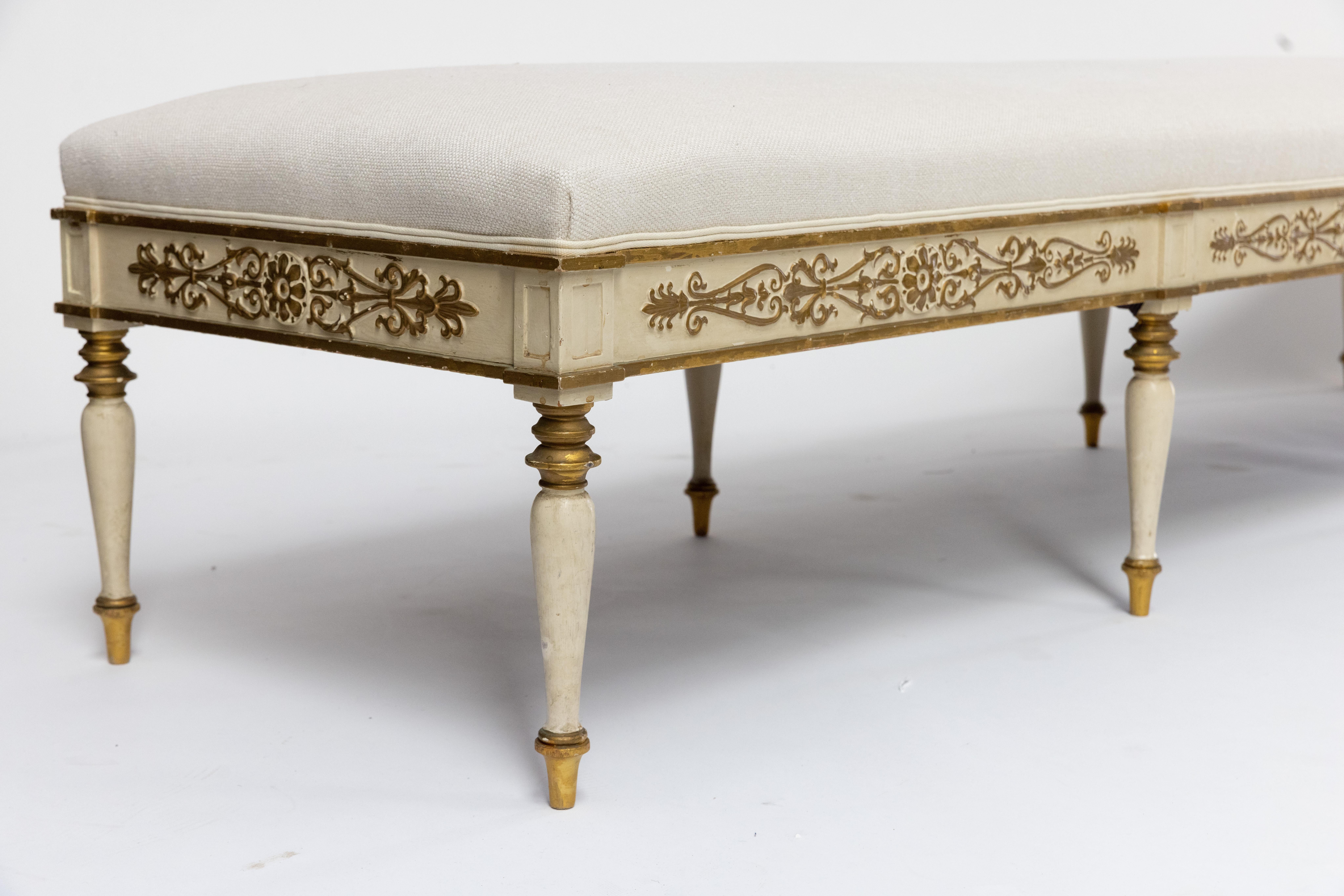 Dekorative und elegante Late Empire Bank mit gepolsterter Sitzfläche. Rahmen aus Buche mit originaler weißer Farbe und zarten, vergoldeten Schnitzereien. Er ruht auf eleganten, gedrechselten, spitz zulaufenden Beinen mit vergoldeten Details an der