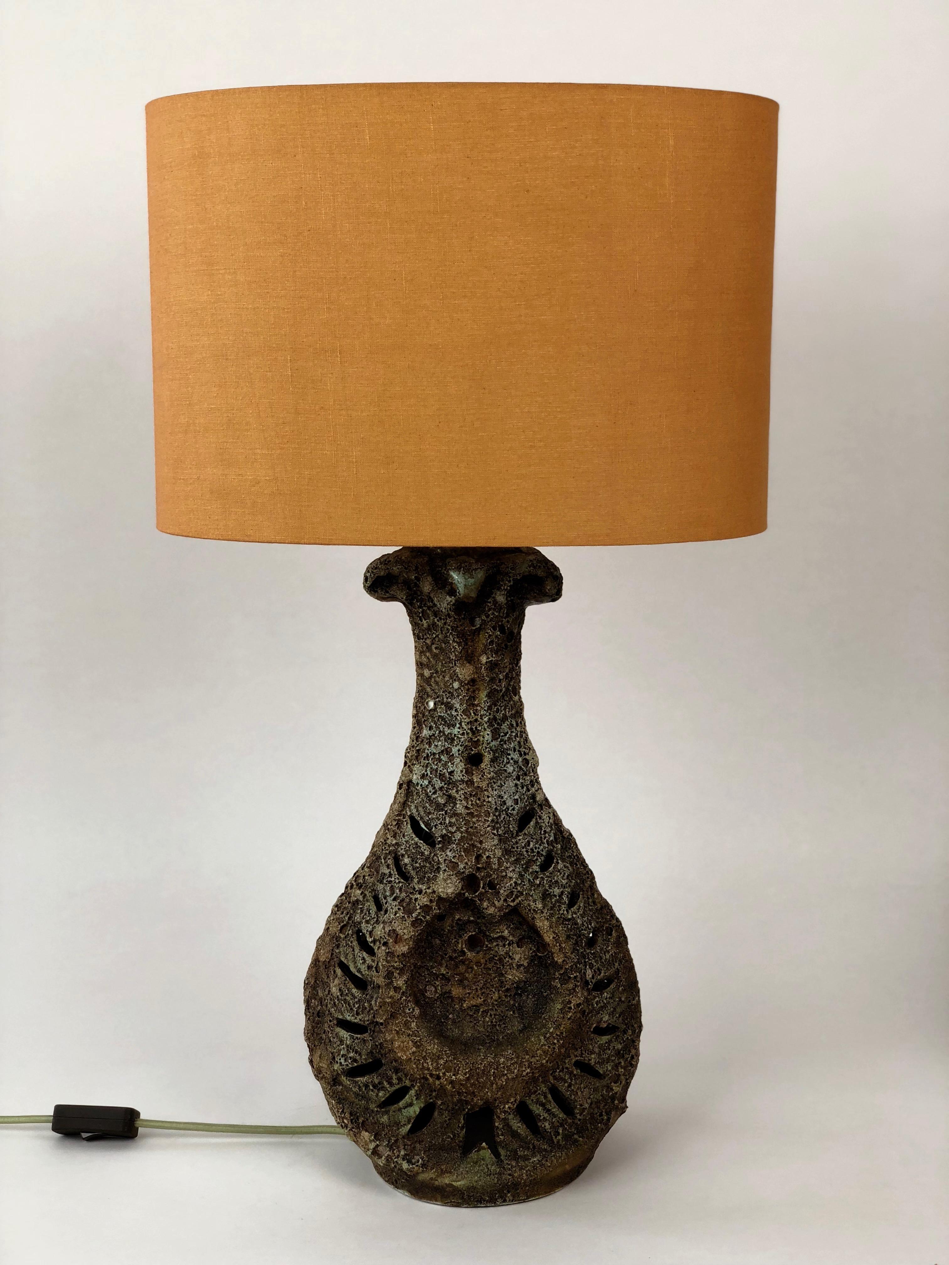 Large and dramatic table lamp made from ceramic with a lava glaze.
The lamp shade is oval in form and in burnt orange linen.
The base also has a light bull inside. When illuminated the lamp has a big dramatic effect.
The lamp is rewired with a