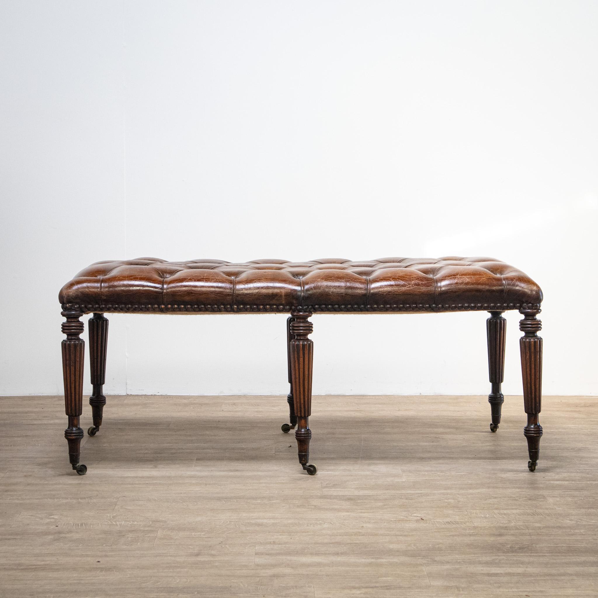 A beautiful quality piece, this large stool has six reeded and turned tapering mahogany legs on brass castors and a lovely chestnut brown buttoned cushion which has a great polished shine to it and large upholstery tack heads around the border. The
