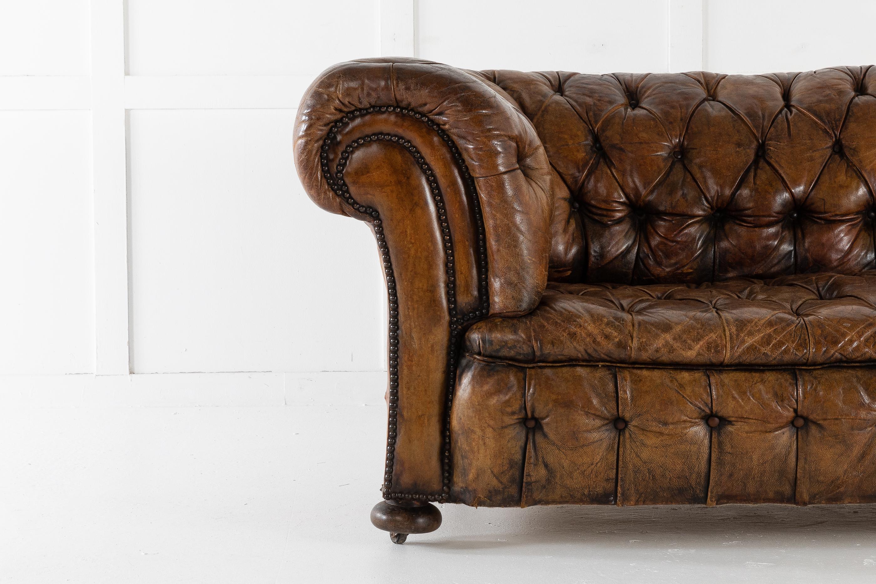Excellent quality, timeless, deep buttoned leather chesterfield retaining its original faded patinated leather. Standing on round wood bun feet. Having brass nailhead trim and fully buttoned base.

Originally in our office for years, very