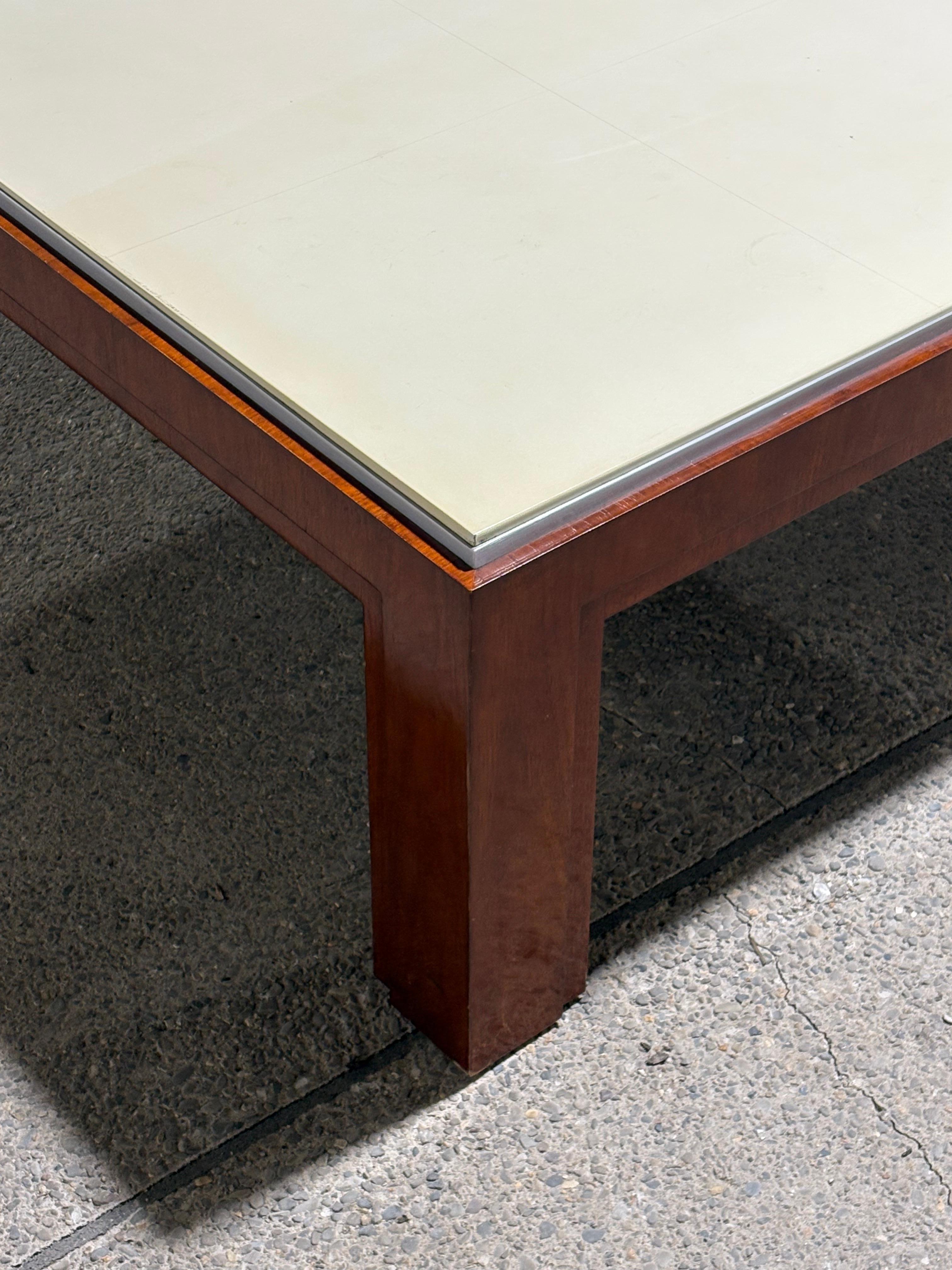 Beautiful and modern square coffee table with cream leather top and thick cherry wood frame. Aluminum accent border under leather adds elegance. 

The leather top is separated into square panels. 

Some wear on the legs and minor wear on the leather