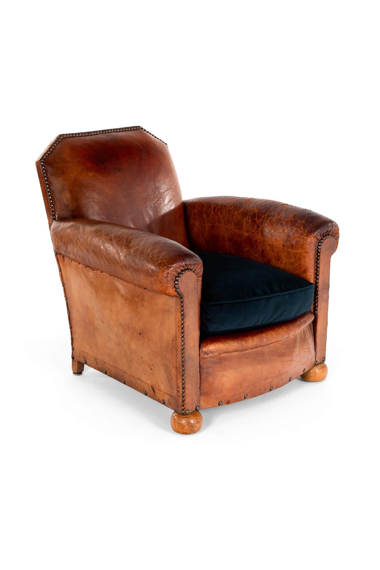 A sumptuous cognac leather club chair with rolled arms and a wide and deep seat. The high deep back is unusual with its symmetrical angular back.

The supple leather with brass studs to the perimeters of the chair and raised on oak bun feet.

Fully
