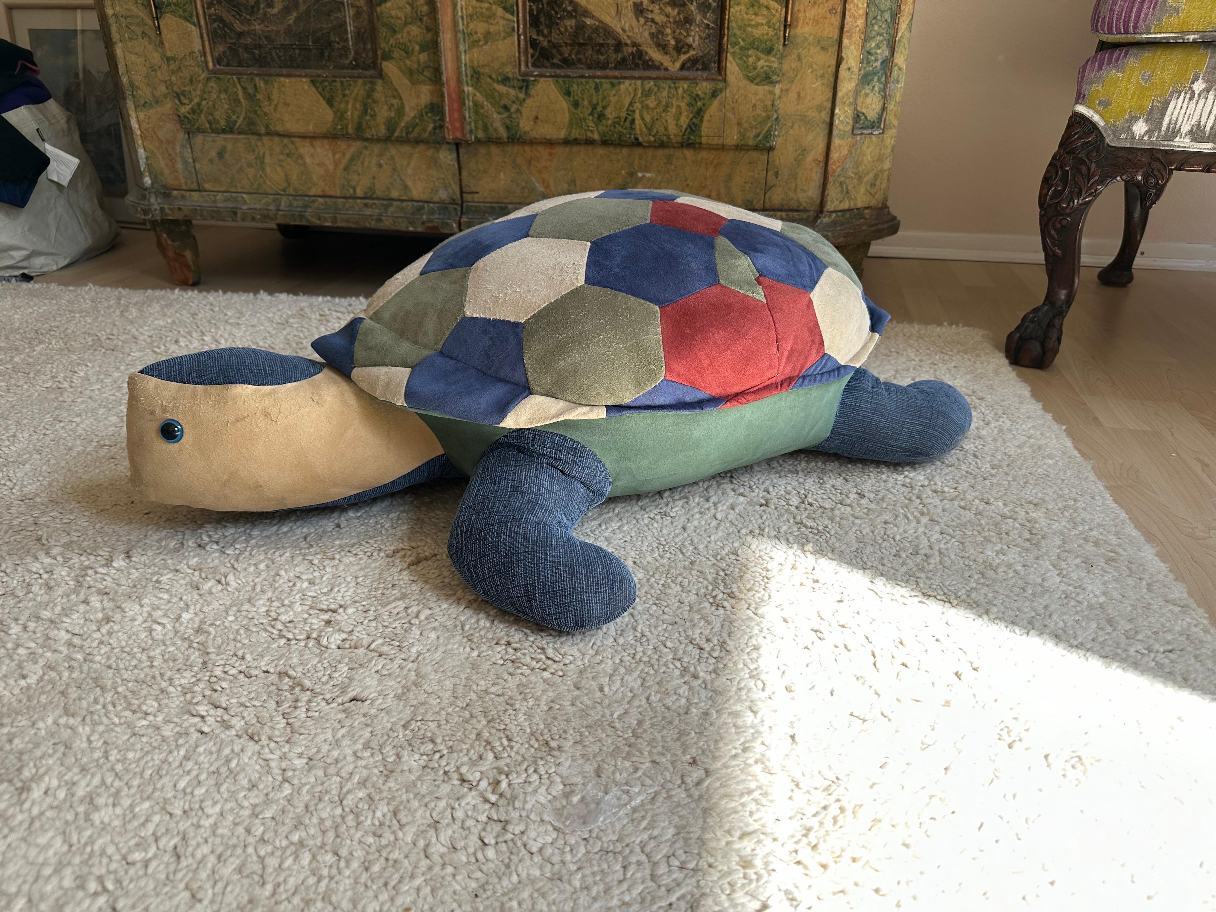 This large leather pouf, crafted in the shape of a turtle, is a charming vintage piece from the 1970s. It features a colorful patchwork shell made from various shades of suede, giving it a playful yet sophisticated look that adds a touch of whimsy