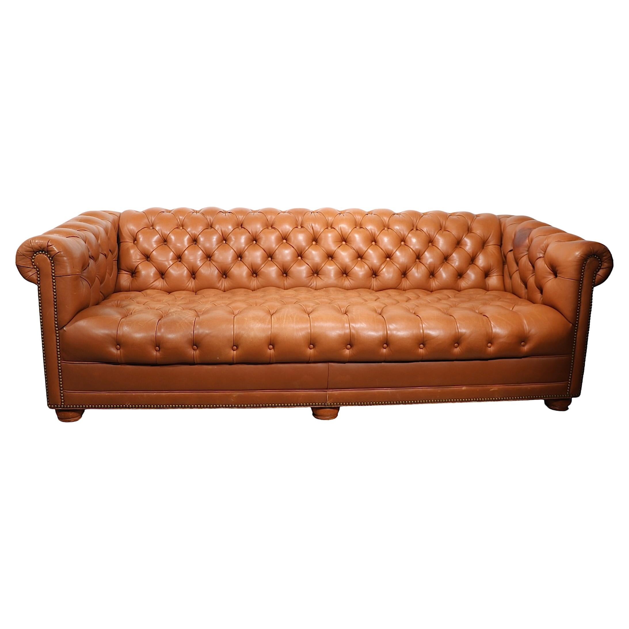 Incredible leather Chesterfield sofa by noted maker. Cabot Wrenn. The sofa feathers an allover tufted seat, back, and arms, with brass nailhead trim, on solid wood bun feet. Super chic, stylish and comfortable, this example does show some wear, and