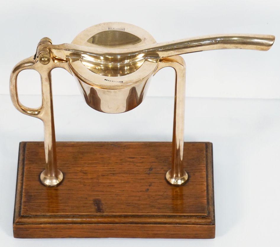 A fine lemon squeeze or citrus juicer for the bar, by the celebrated English silversmiths Mappin and Webb, featuring an apparatus with handle and squeeze of a quality brass and copper alloy mounted to a moulded rectangular wood base, with a