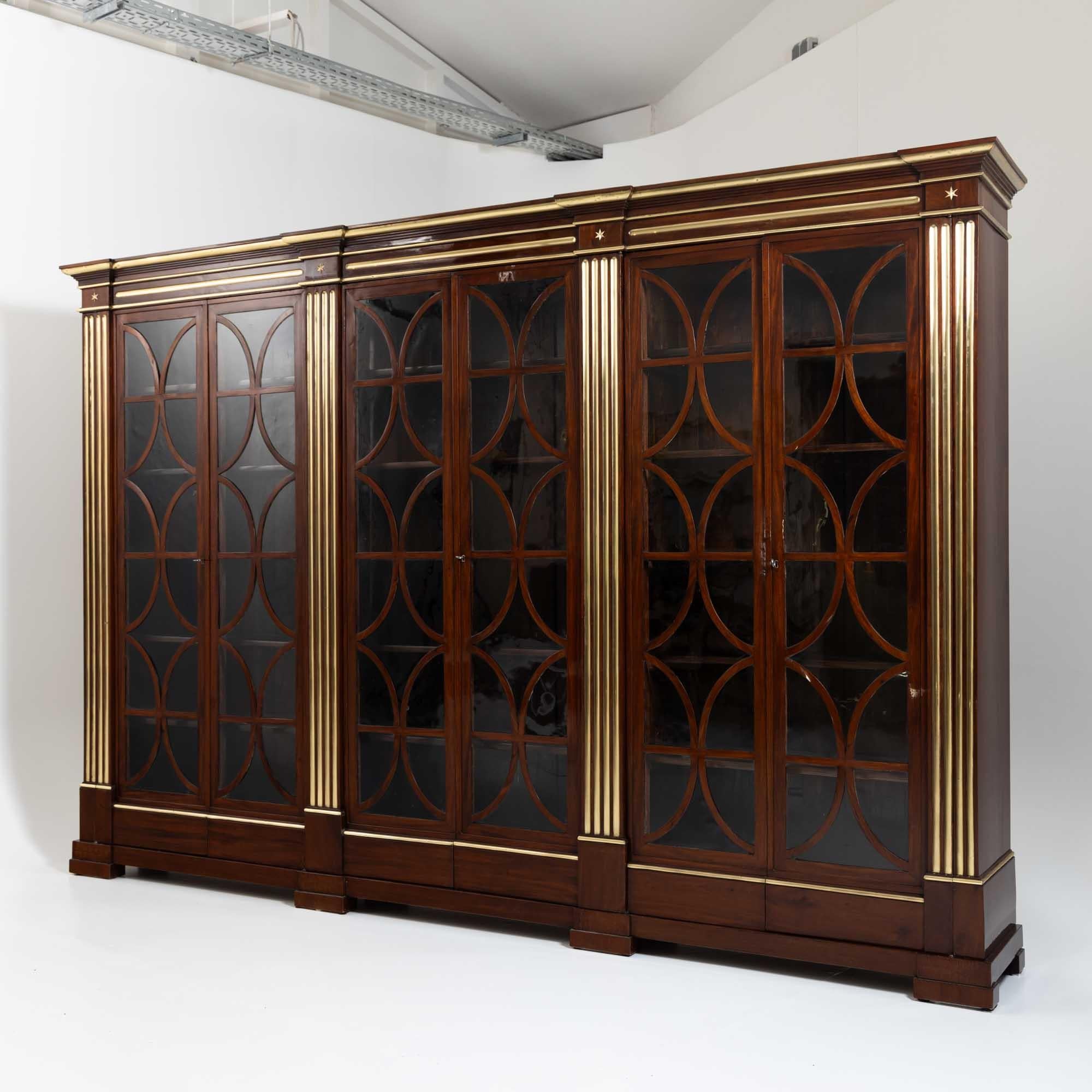 Large six-door library or bookcase with glazed doors with elegant C-shaped glazing bars and dividing pilasters with brass-lined fluting. The library is veneered in mahogany. The straight, multi-profiled cornice is also decorated with brass profiles.