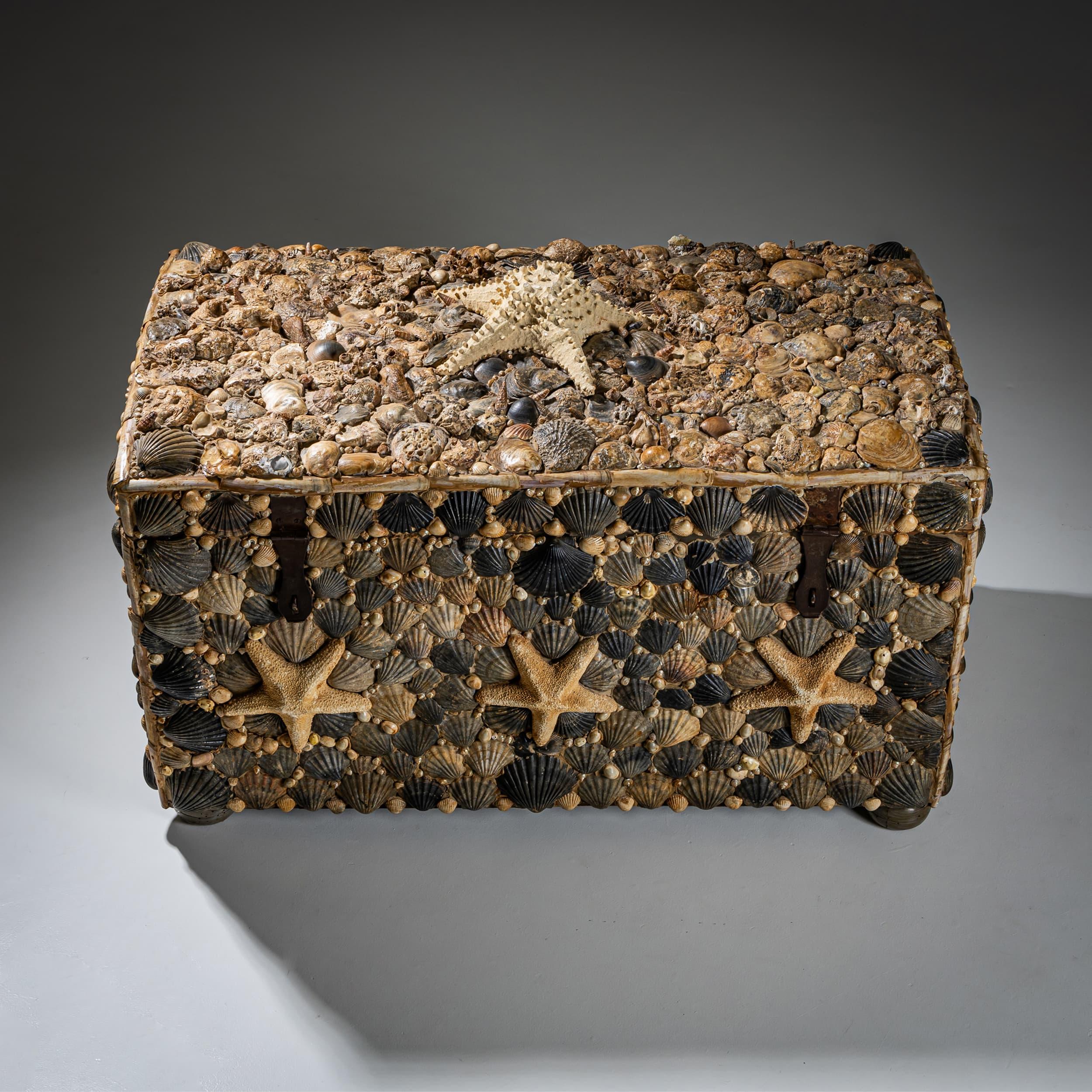 Llamativo cofre del tesoro adornado con conchas marinas aplicadas y prominentes estrellas de mar en la tapa y los paneles laterales. Los herrajes decorativos acentúan el carácter náutico del arcón. Se apoya en pies de bola comprimida, combinando un