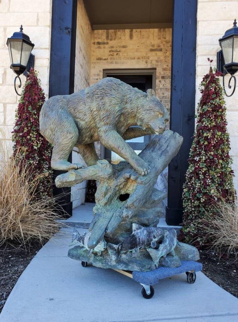 A magnificent outdoor bronze bear and fish statuary, plumbed as a water fountain. The vintage American sculpture depicting a realistic wildlife scene, a frozen moment in time that features a large bear climbing across a naturalistic base of a log