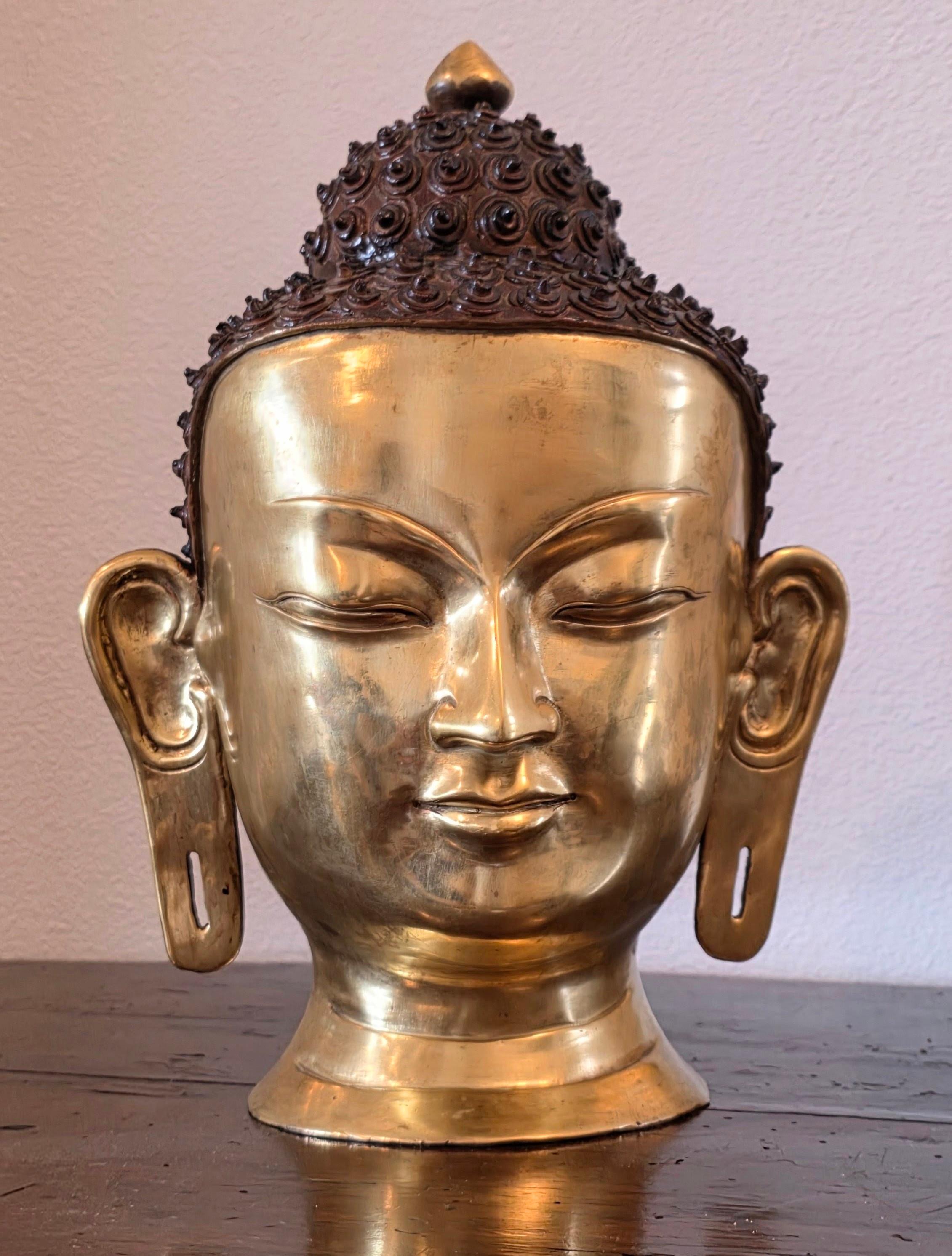 Una testa di Buddha nepalese a grandezza naturale di ottima qualità e di grande impatto visivo, con una patina calda e ben invecchiata. 

Eccezionale esecuzione in ottone/bronzo con finitura brillante in oro dorato/rame antico. Quasi certamente