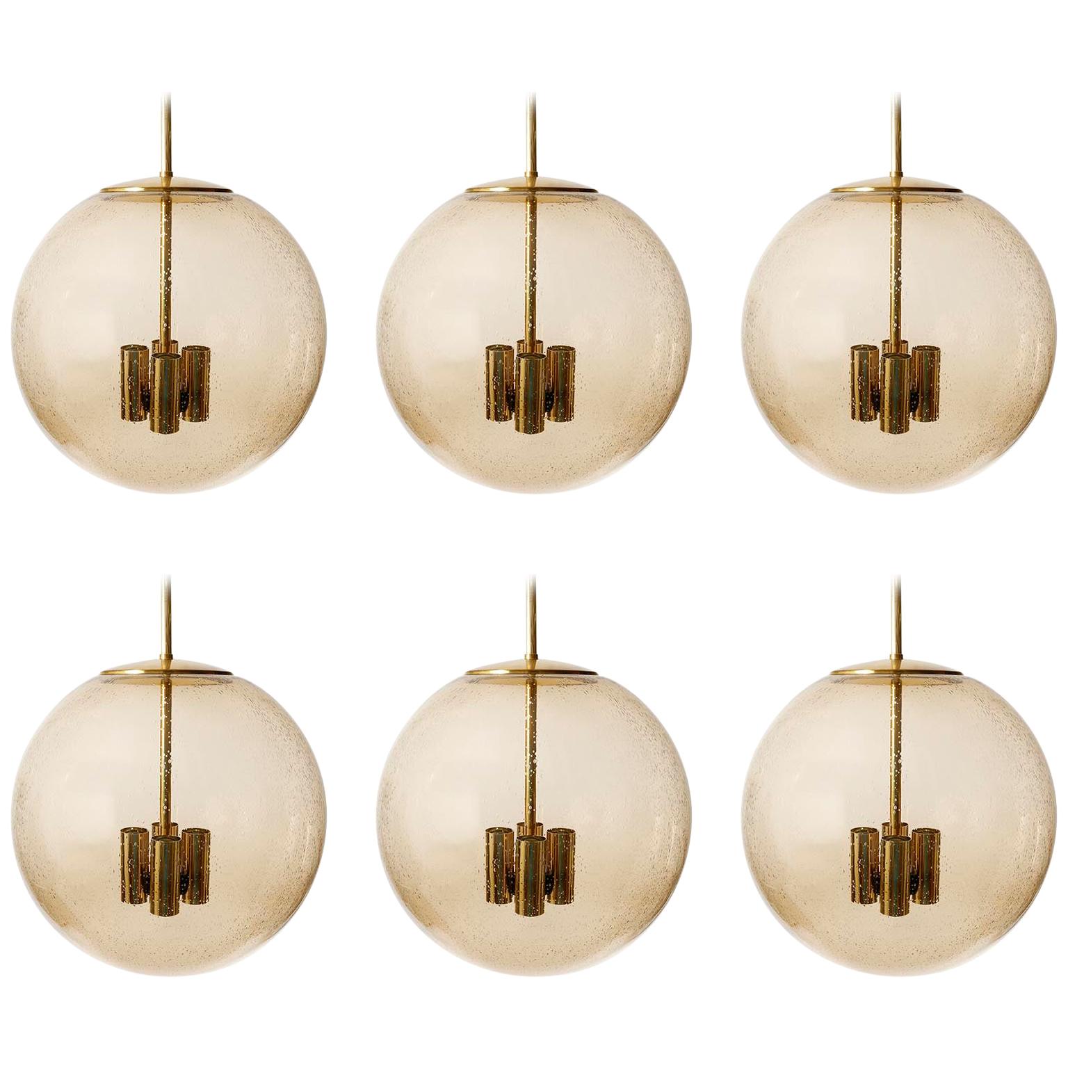 One of six extra large brass and hand blown glass globe pendants model 'P 197' by Glashütte Limburg, Germany, manufactured in midcentury, circa 1970.
The armature, rod and canopy are made of polished brass. The seeded glass globe with many air