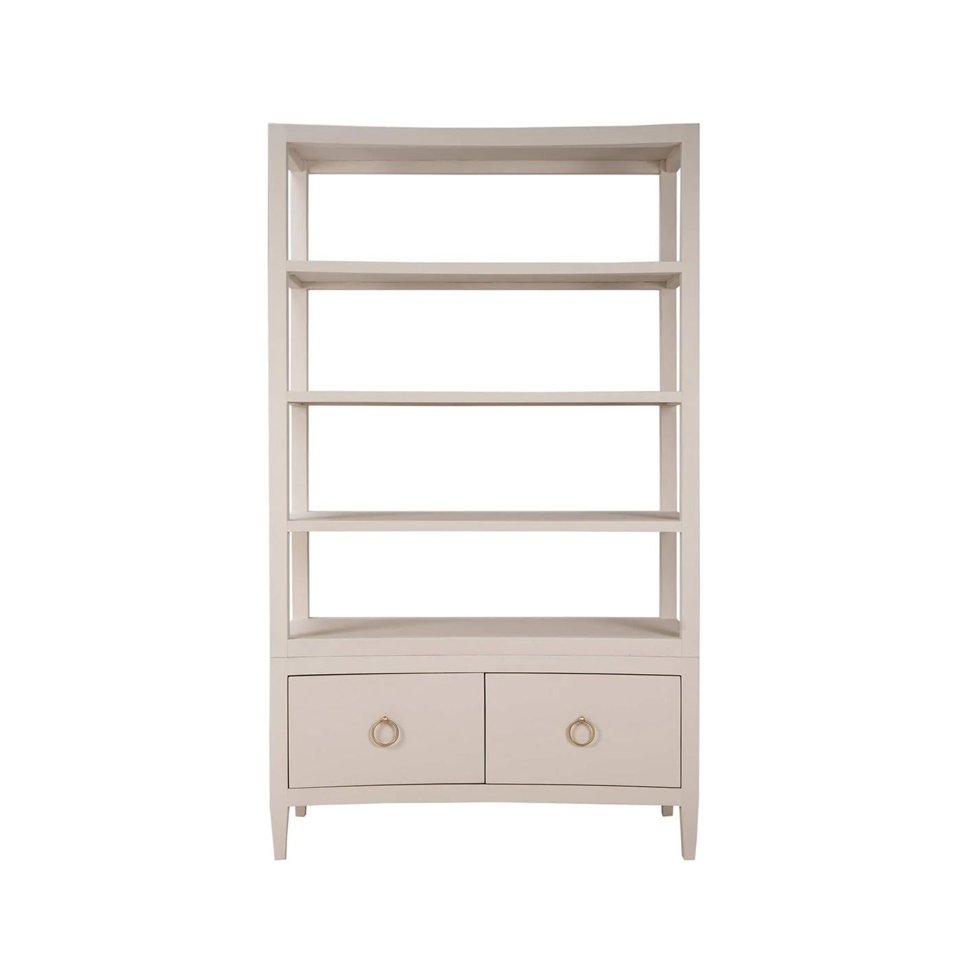 Wrapped in soft ivory putty color linen, this tall shelving unit features a subtly concave front that introduces movement and elegance to its minimalist profile. Four open shelves offer ample space for display, while two lower drawers with ring-pull