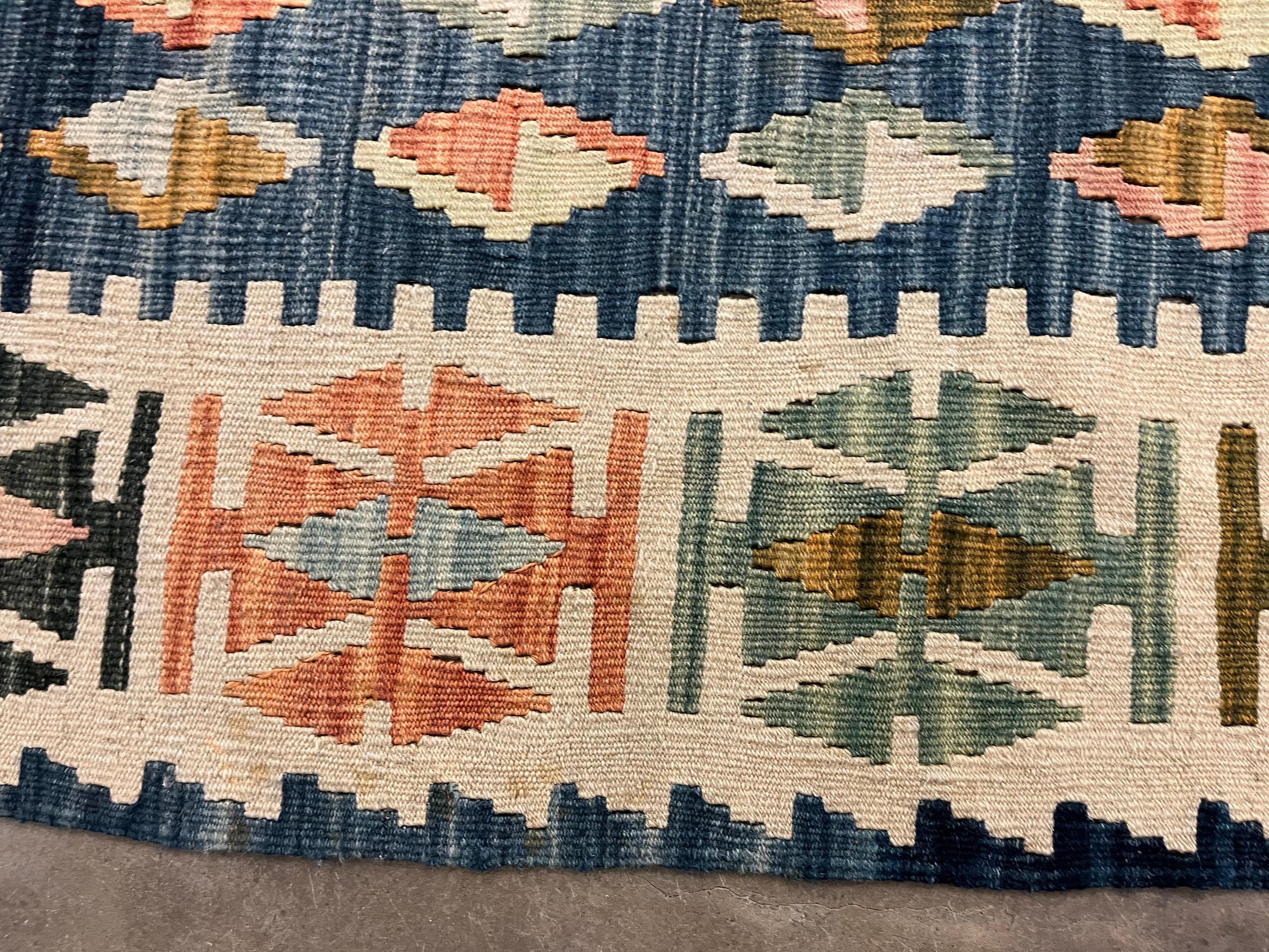 This vintage 1920s Turkish Kilim rug is a large-format flatweave featuring bold geometric artistry in a vibrant multicolour palette. Handwoven from natural wool, it displays repeating zig-zag and diamond motifs in earthy beige, cream, blue,