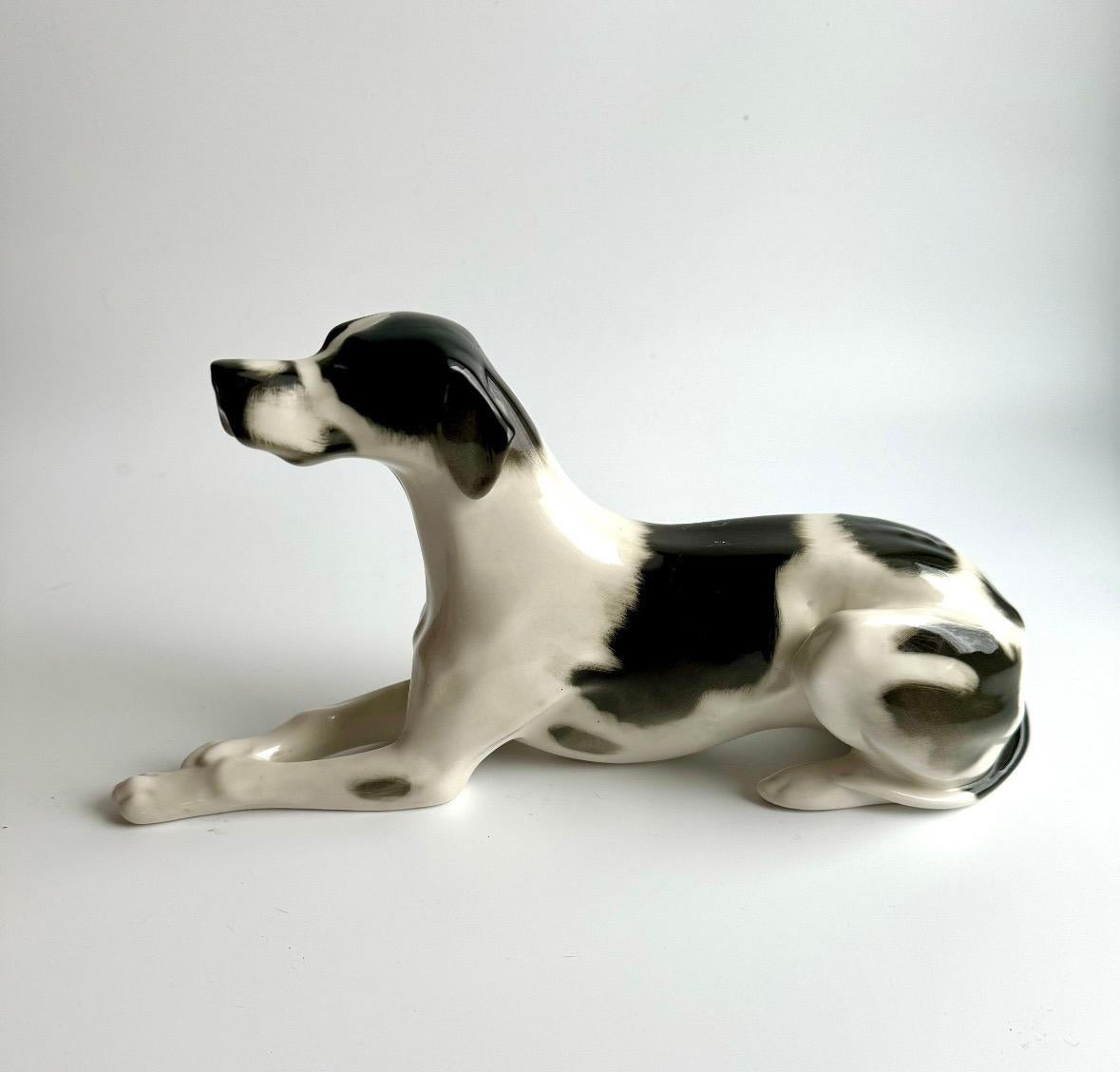 Evoke the timeless grace of classic English charm with this exquisite porcelain English Pointer dog figurine. Perfectly captured in a serene resting pose, this large statuette showcases the elegant lines and dignified expression characteristic of