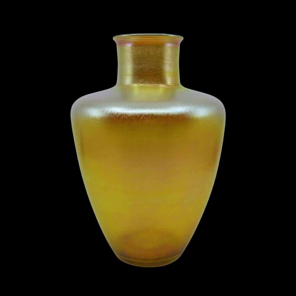 Nous vous proposons ce grand vase en verre d'art Louis Comfort Tiffany Favrile doré et irisé. Ce vase présente une forme d'urne effilée avec des épaules profondes, un col cylindrique et une bouche évasée. Il est irisé d'or avec de belles nuances de