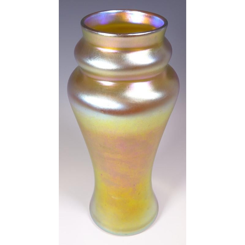 Offering this large Louis Comfort Tiffany gold Favrile iridescent art glass vase. This vase features a double gourd design, flared, cylindrical body finished in gold iridescence with beautiful magenta and platinum hues. Signed on the underneath 