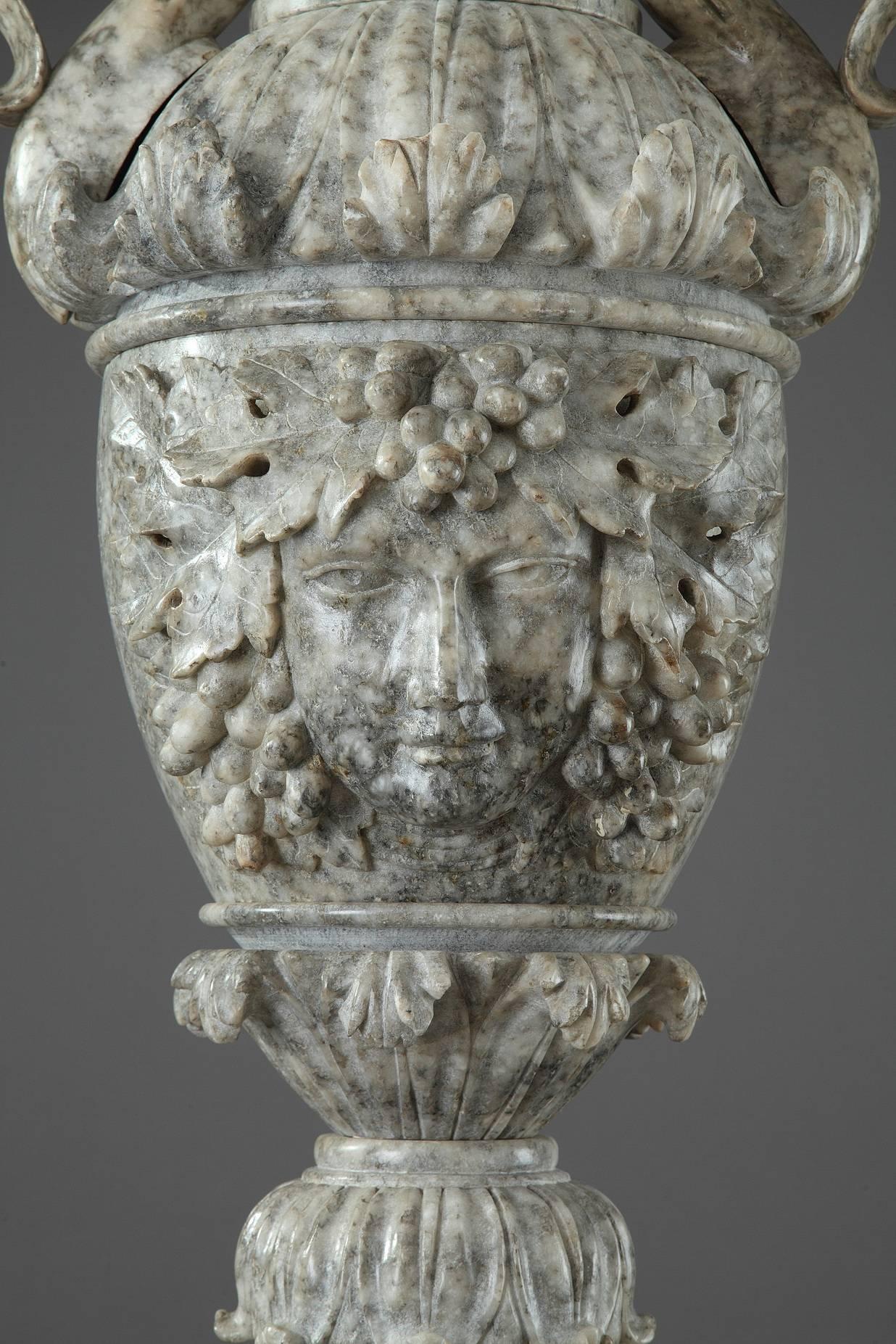 Sumptuous French alabaster pedestal crafted in the first half of the 19th century. Taking the form of an architectural column, this antique pedestal is topped by an urn accentuated with Bacchus head, acanthus and lotus leaves. The urn is flanked by