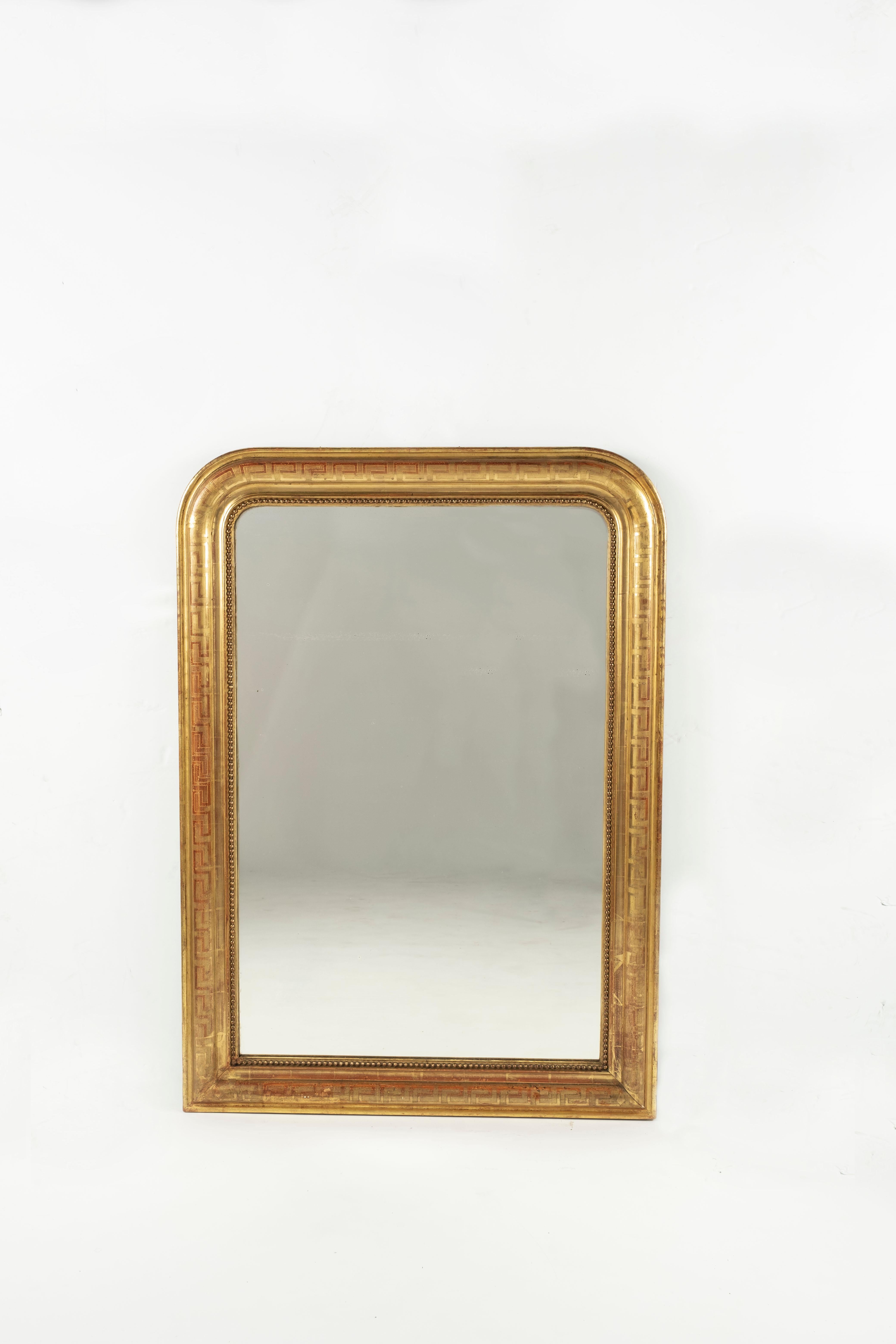 A 19th century French overmantle/ wall mirror. The original gilding is in excellent condition with a decorative Greek key design to the surface. Over a century of natural wear has revealed the reddish bole base coat beneath creating a pleasing