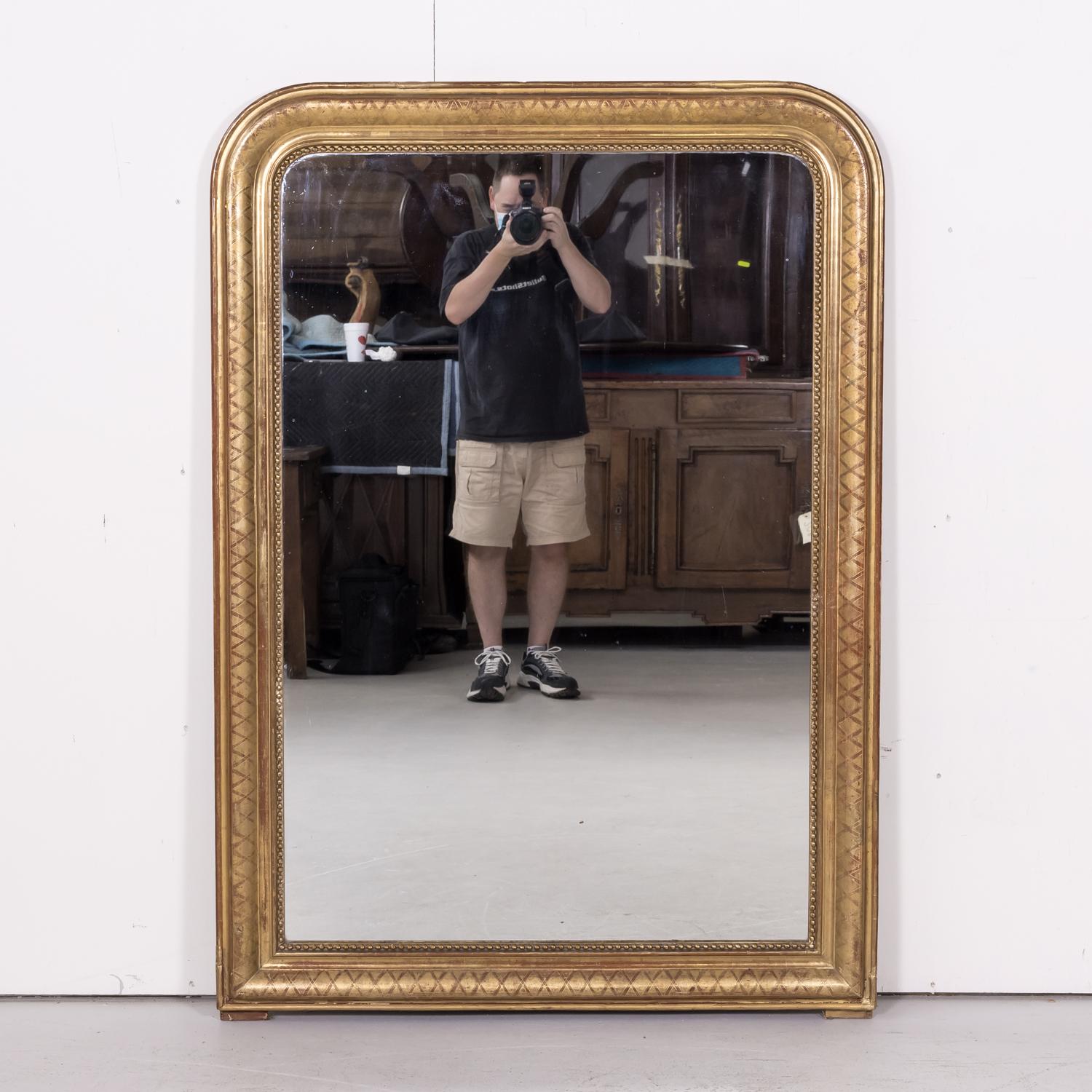 A large 19th century French Louis Philippe period giltwood mirror having its original mercury glass and cross hatch etching to the frame, circa 1840s. The tall rectangular shape of the frame has straight corners at the base, while the upper