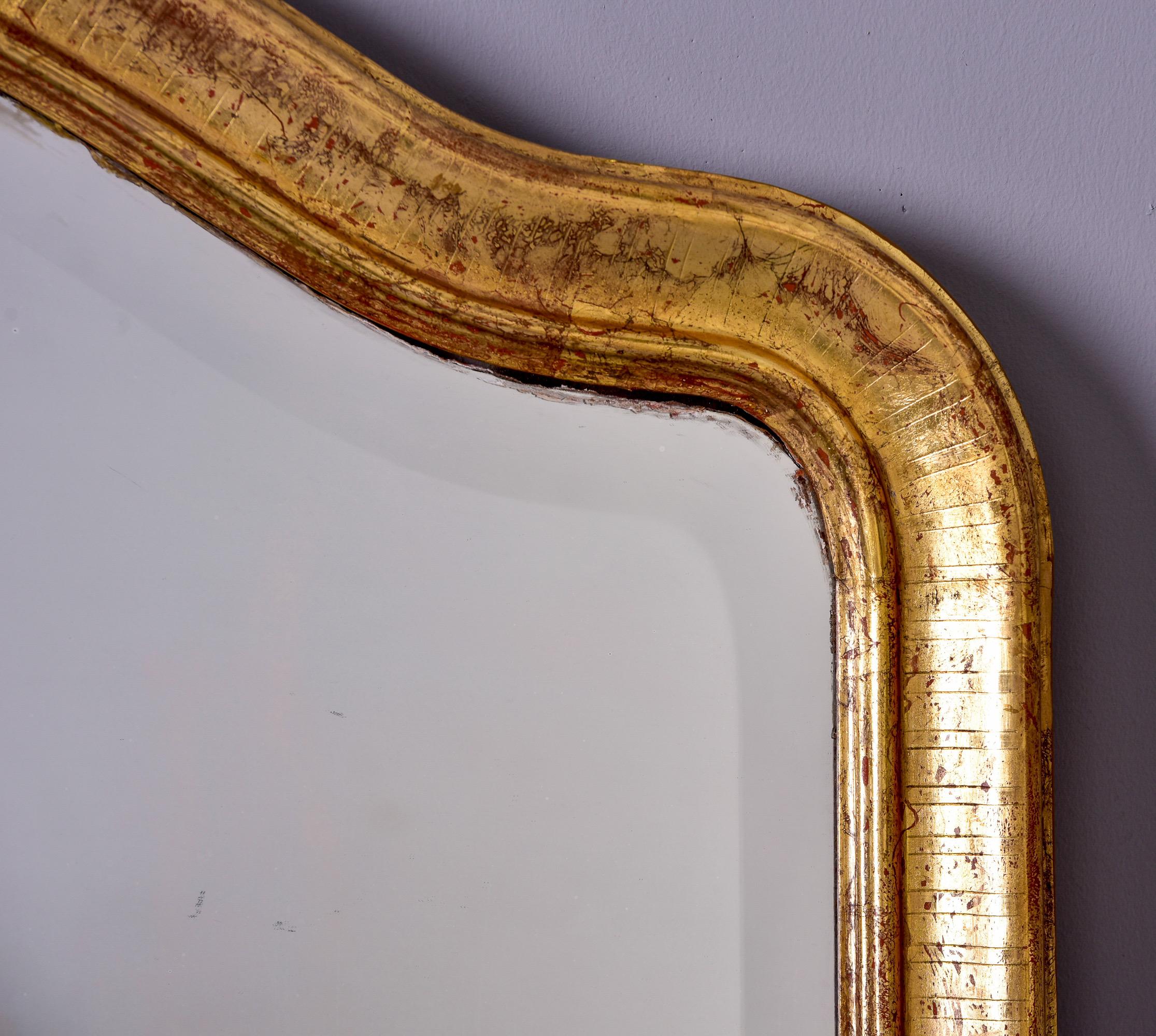 Circa late 19th century tall gilded Louis Philippe mirror with decorative crest and beveled edge. Unknown maker. 

Overall very good antique condition with some scattered surface wear to wood and mirror.