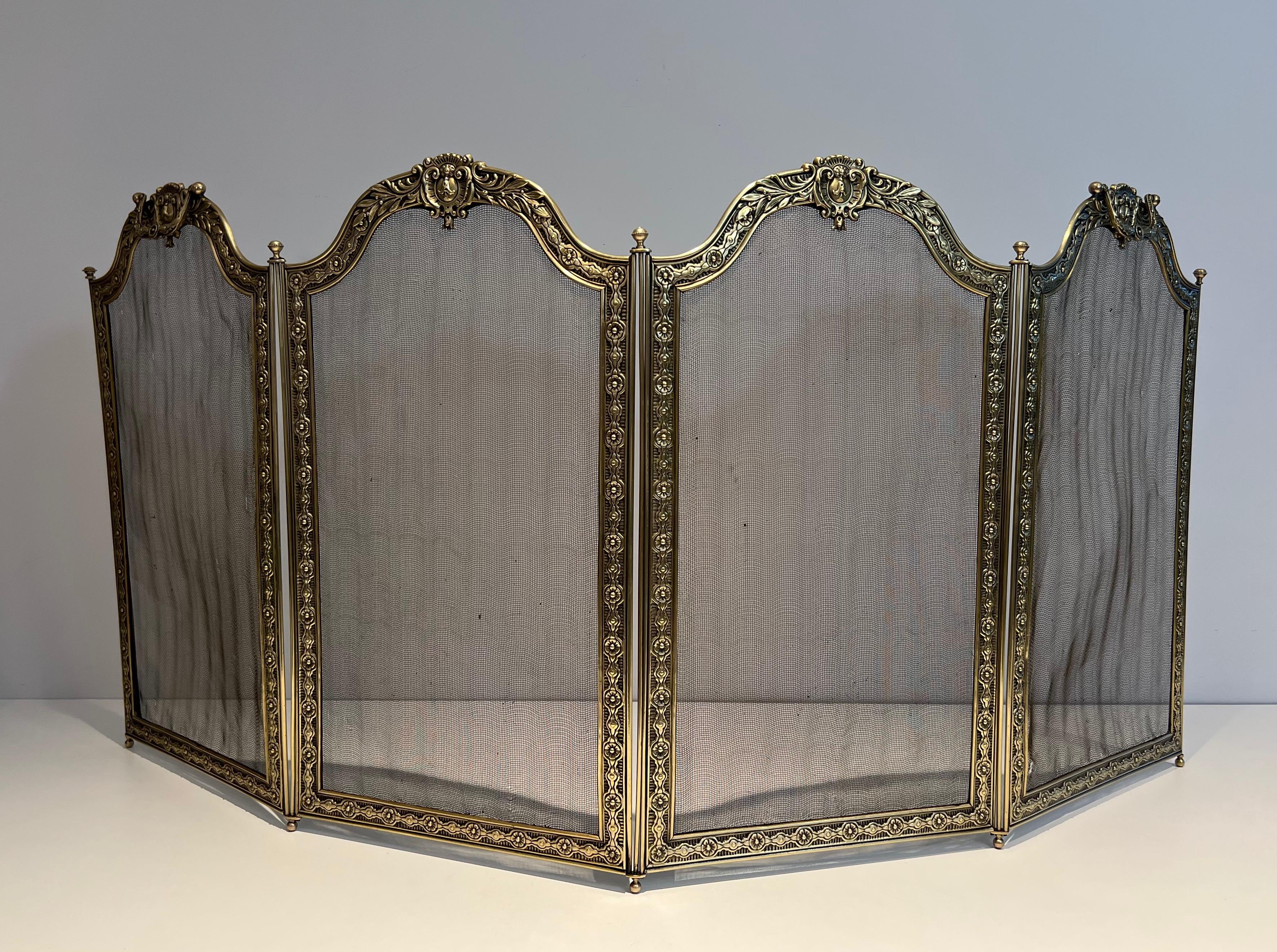 This large folding fireplace screen with 4 grilling panels and framed by an embossed brass and bronze frieze is decorated with macaroons and garlands decorated with rosettes. It has 2 removable handles. This is a French work in the Louis XVI Style.