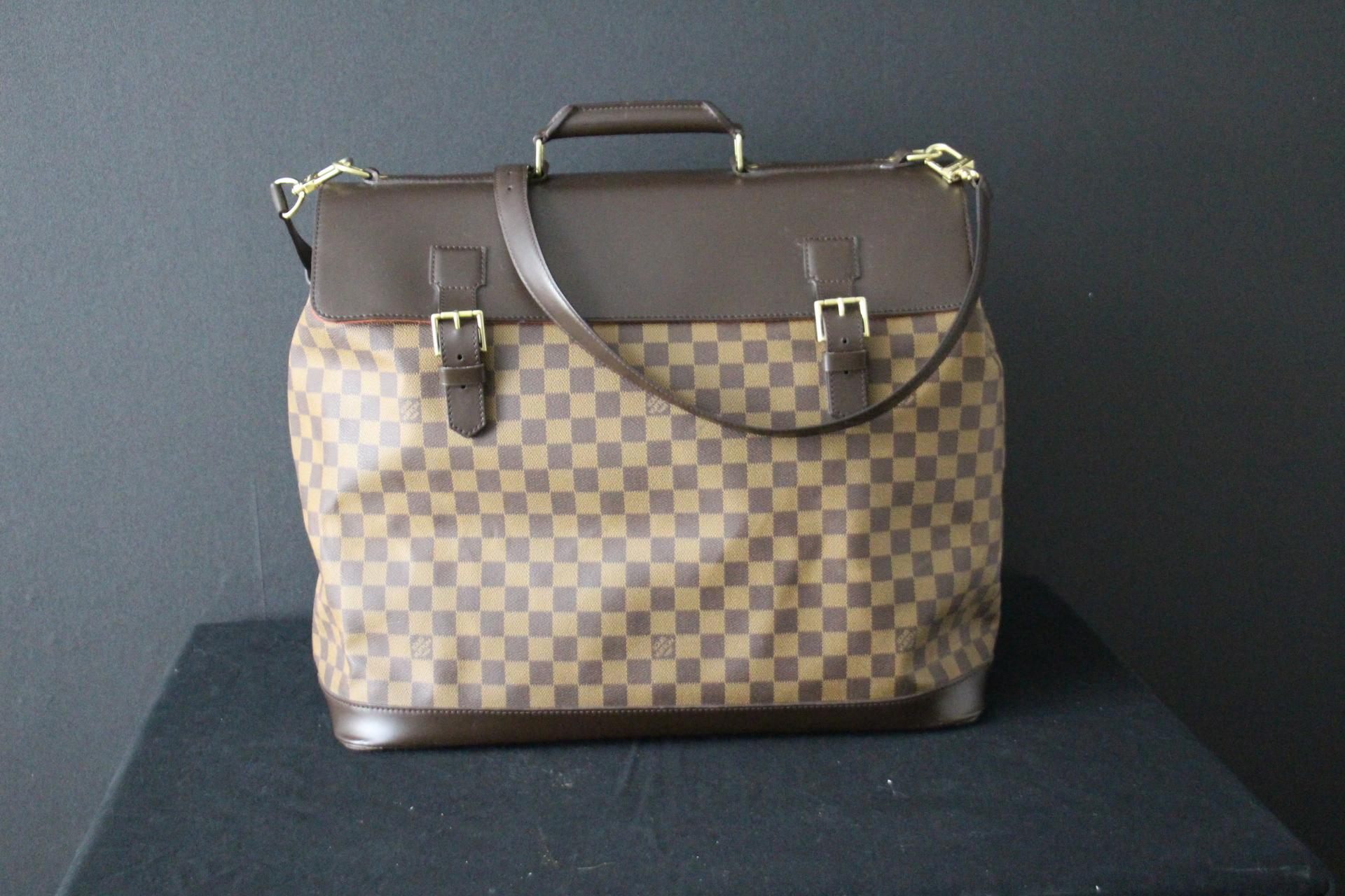 This beautiful large Louis Vuitton bag features the very sought after ebene damier canvas body with leather trim, a flat top handle, a detachable and adjustable leather shoulder strap, a flap top with belt buckle closures, and an back zip pocket.