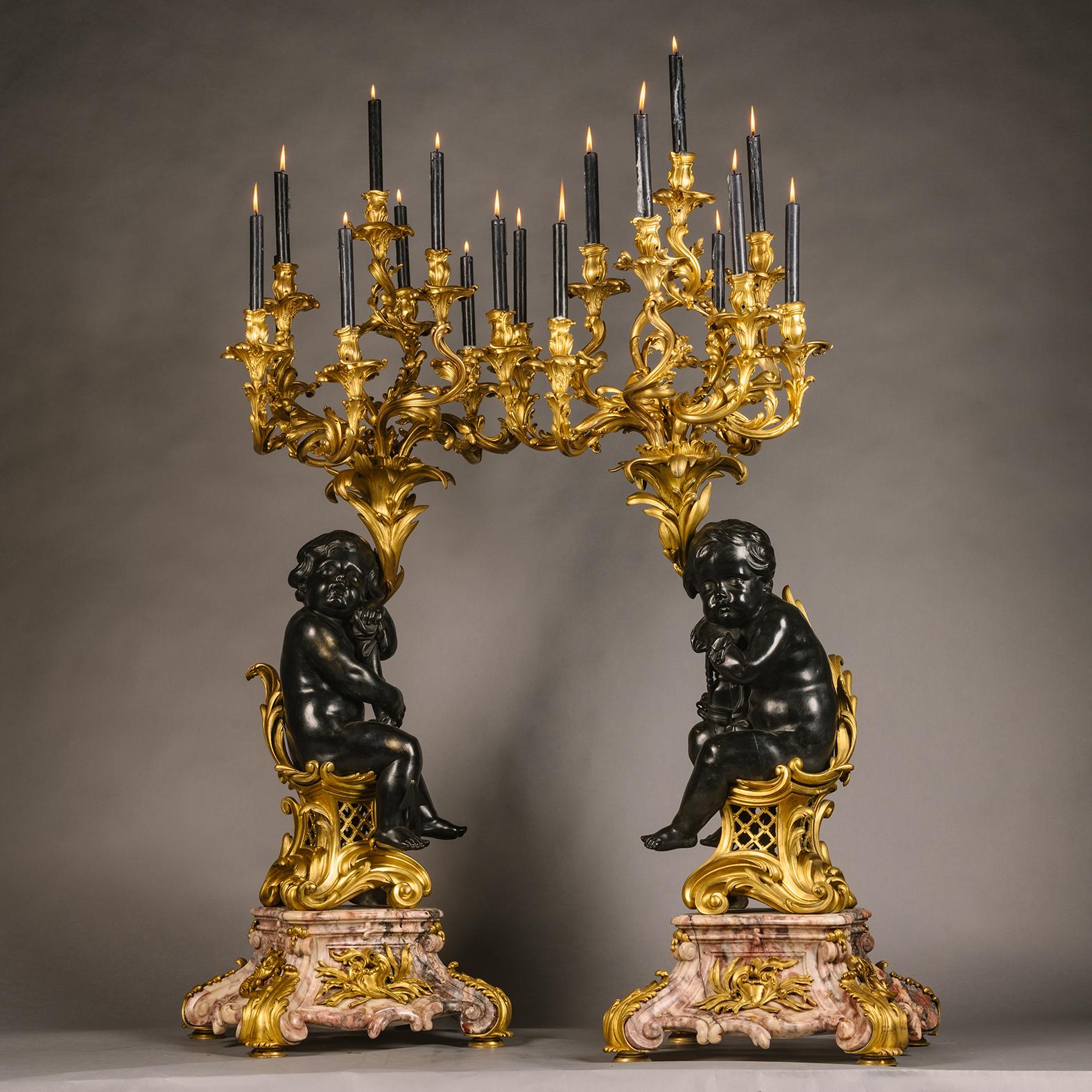A pair of Large Louis XV Style Gilt and Patinated Bronze and Marble Figural Candelabra. 

Each modelled with naturalistically cast rocaille and laurel leaf candle branches above cherubs, one holding an anchor and the other an hourglass, seated on