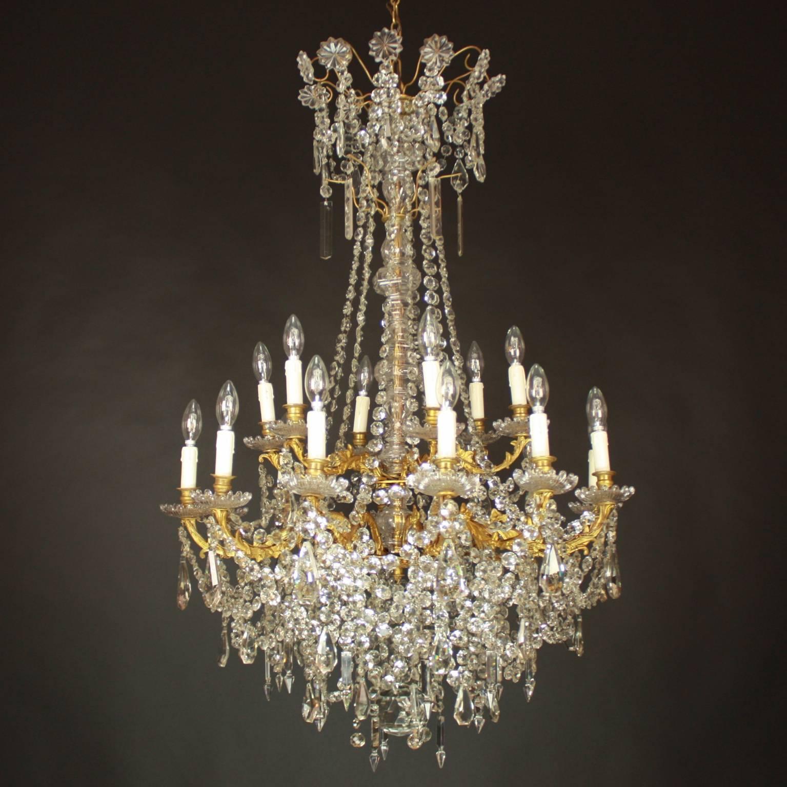 A Large Louis XV style gilt-bronze and cut-crystal eighteen light chandelier, with a central cut-crystal baluster stem issuing two rows of gilt-bronze branches finally cast and chased with foliage. The branches support gilt-bronze nozzles with glass