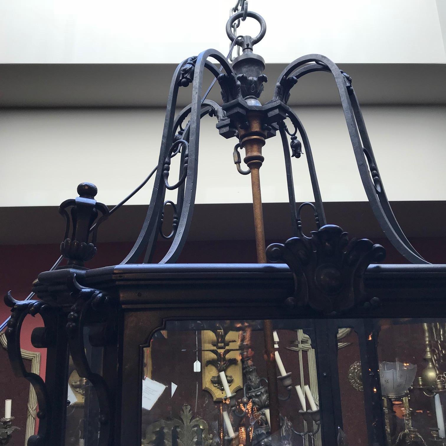 Very large hand-wrought Iron Louis XV style lantern with a two-tier gilded iron
twelve-light interior chandelier encased by four large beveled glass panes and four corner angled beveled panes.
Wrought Iron detailing and finials top and bottom.