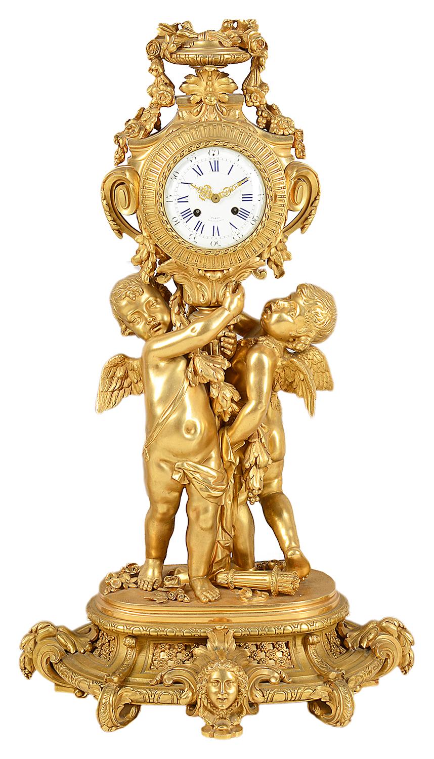 A very impressive gilded ormolu Louis XVI style clock garniture, the clock and candelabra being supported by winged cherubs, scrolling swags and foliage and classical mask mounts. The enamel clock face with an eight day duration movement that chimes